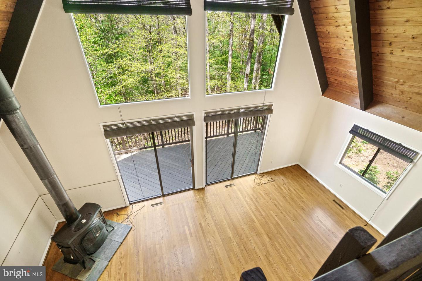 Living room with a wood-burning stove, tall windows, hardwood floors, and a wooded view.