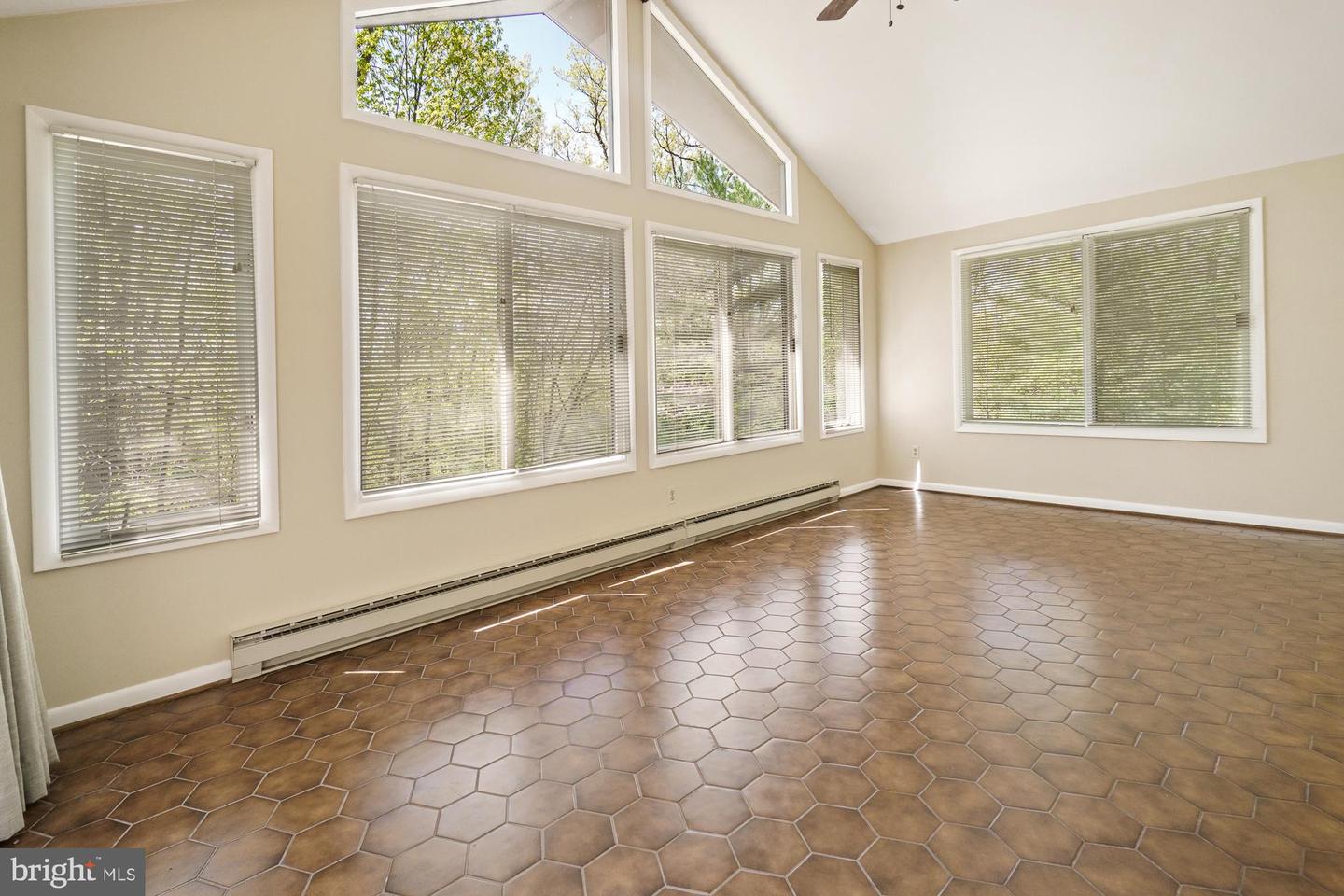 Empty room with vaulted ceiling, broad windows, and brown hexagonal tile flooring.