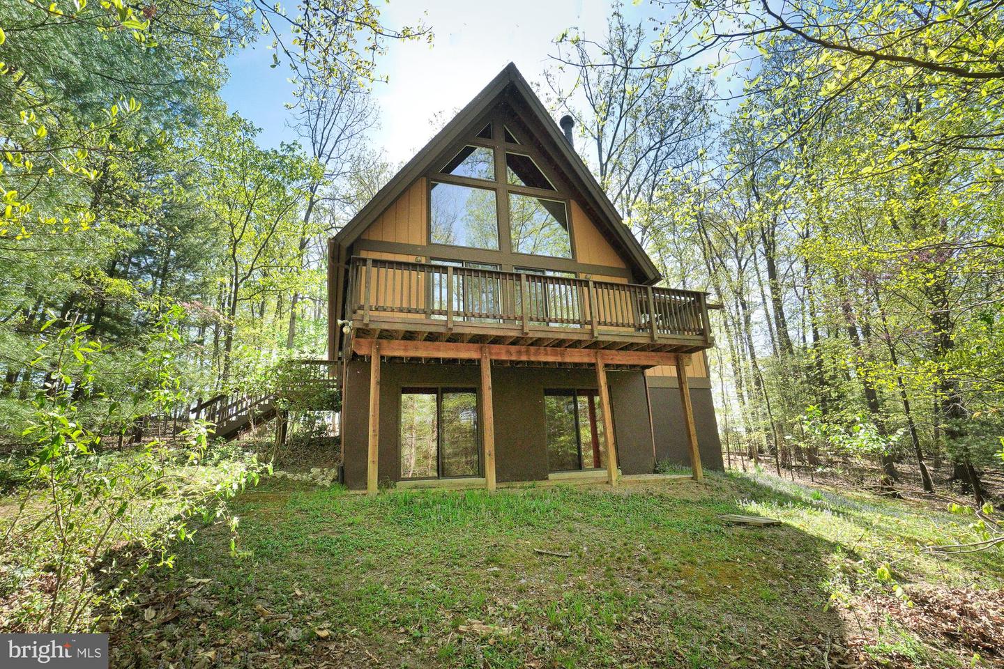Wooded A-frame house with a long elevated rear deck and large triangular windows.