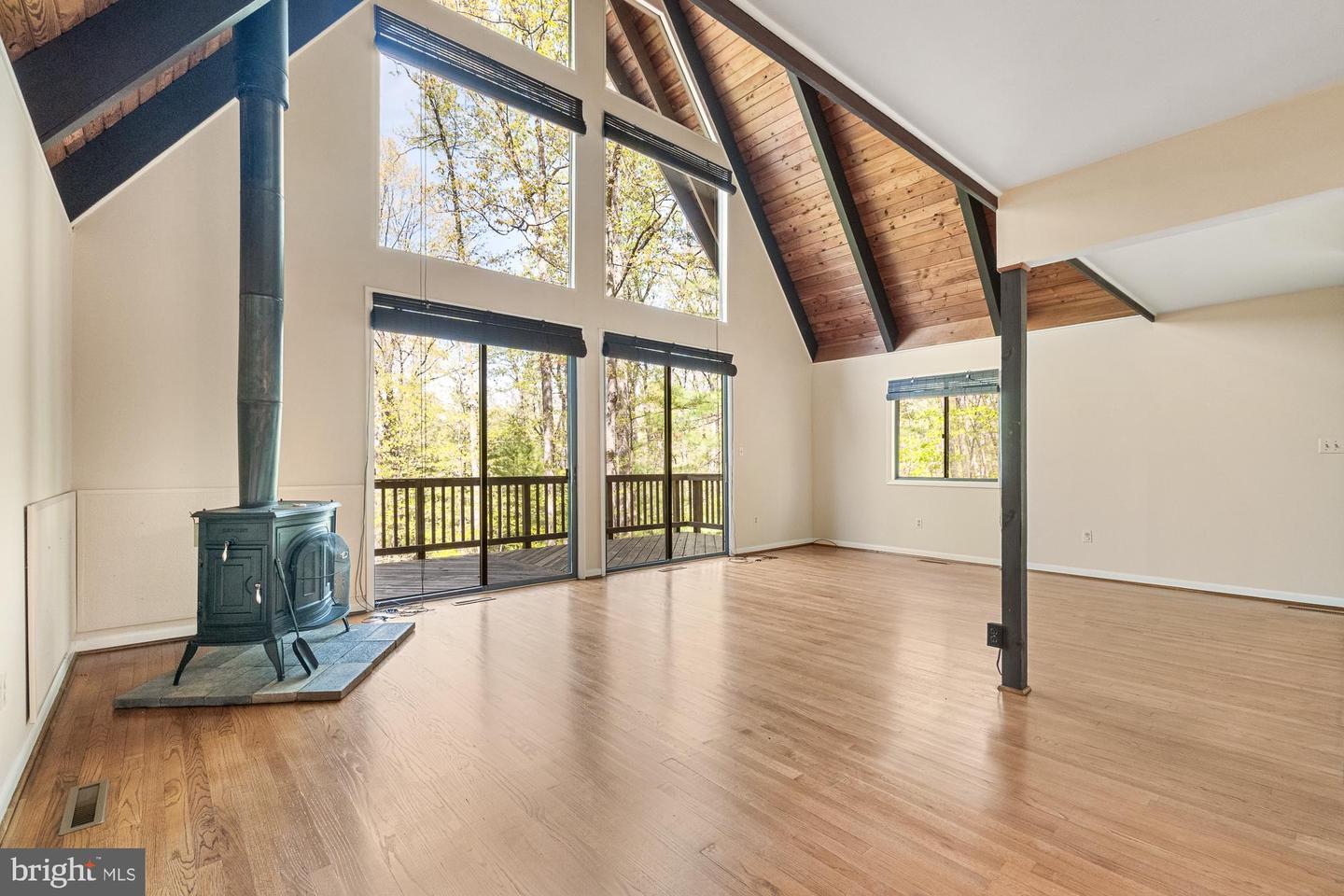 Living room with vaulted wood ceiling, tall windows, deck access, and a freestanding wood stove.