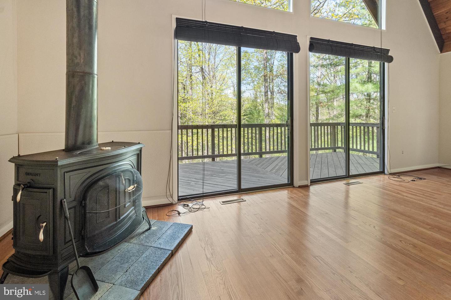 Living room with a freestanding wood stove and tall glass doors opening to a wooded deck.