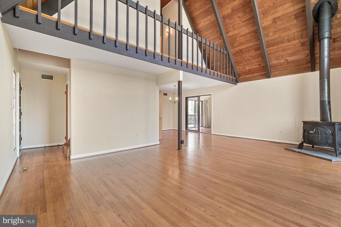 Living room with a vaulted wood ceiling, open loft railing, hardwood floors, and wood-burning stove.