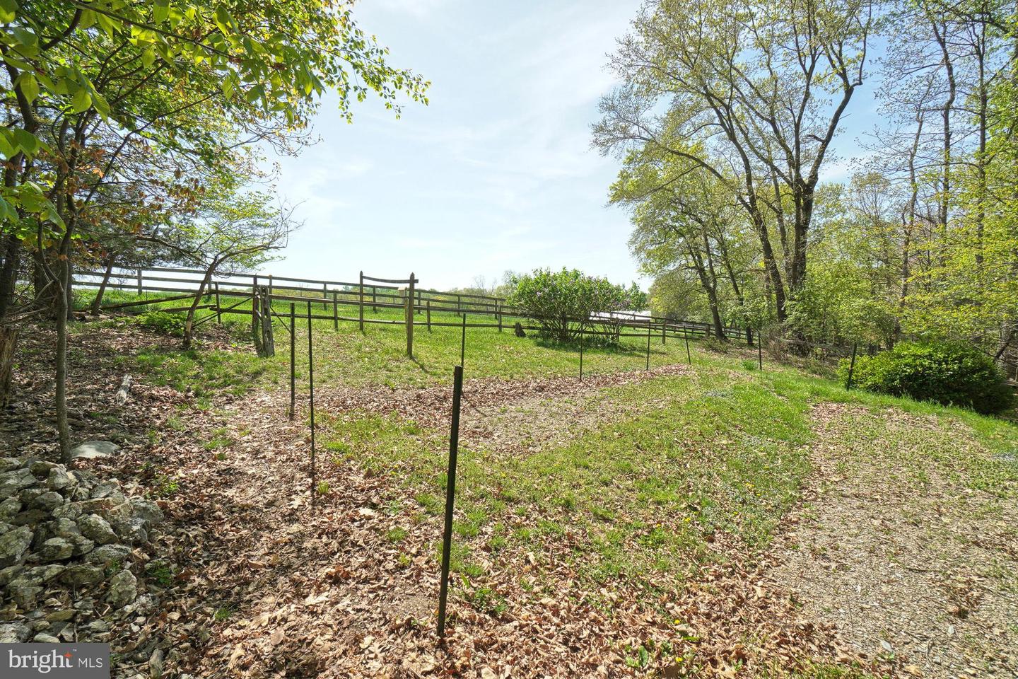 Grassy property lot with wooden and wire fences, mature trees, and a stone border.