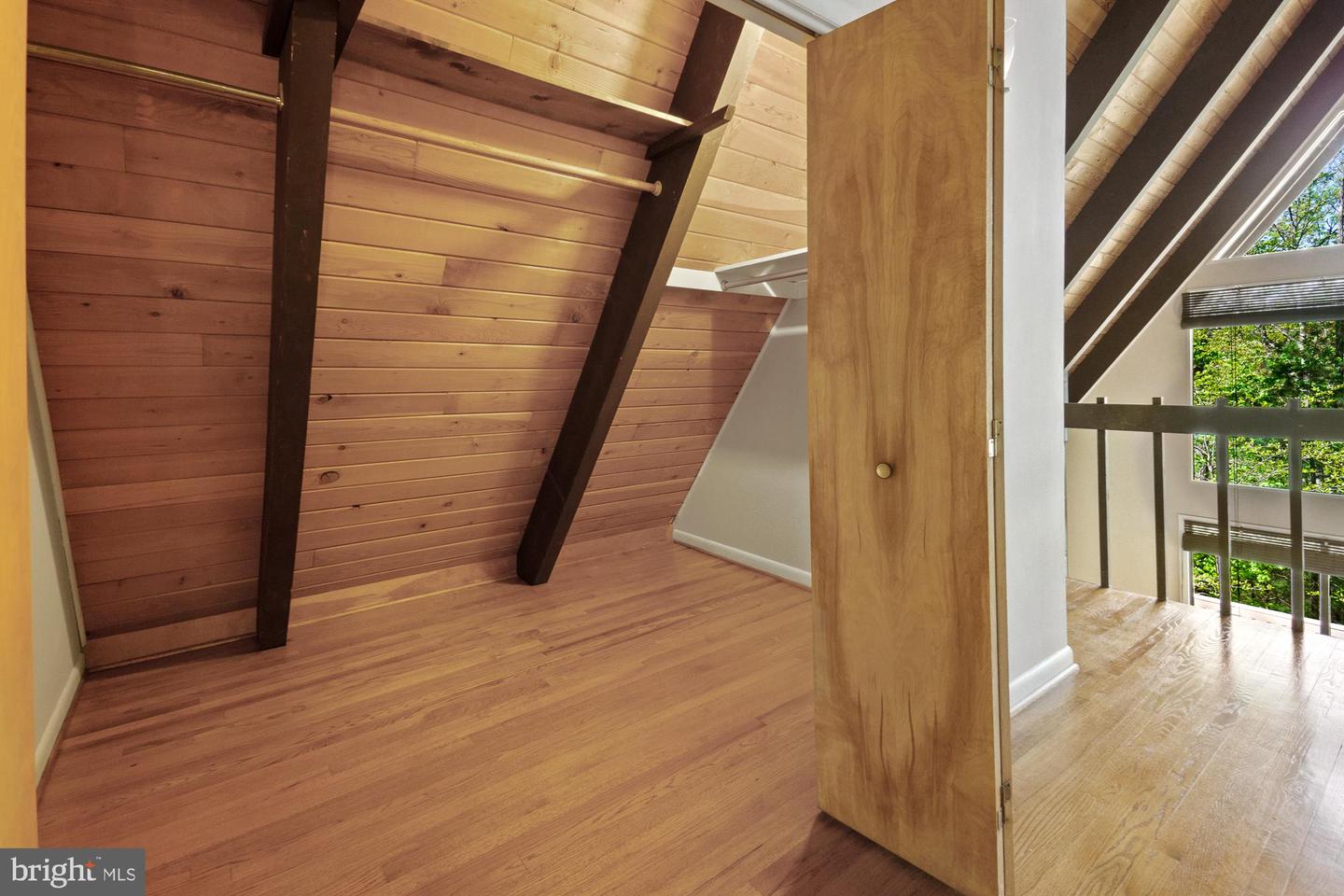 Finished attic loft with sloped wood ceilings, exposed beams, and an open doorway to a bright landing.