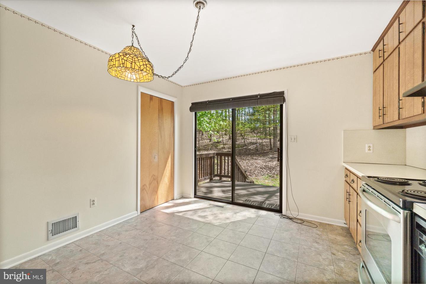 Unfurnished kitchen with wood cabinets, tiled floor, and sliding glass door to a wooded deck.