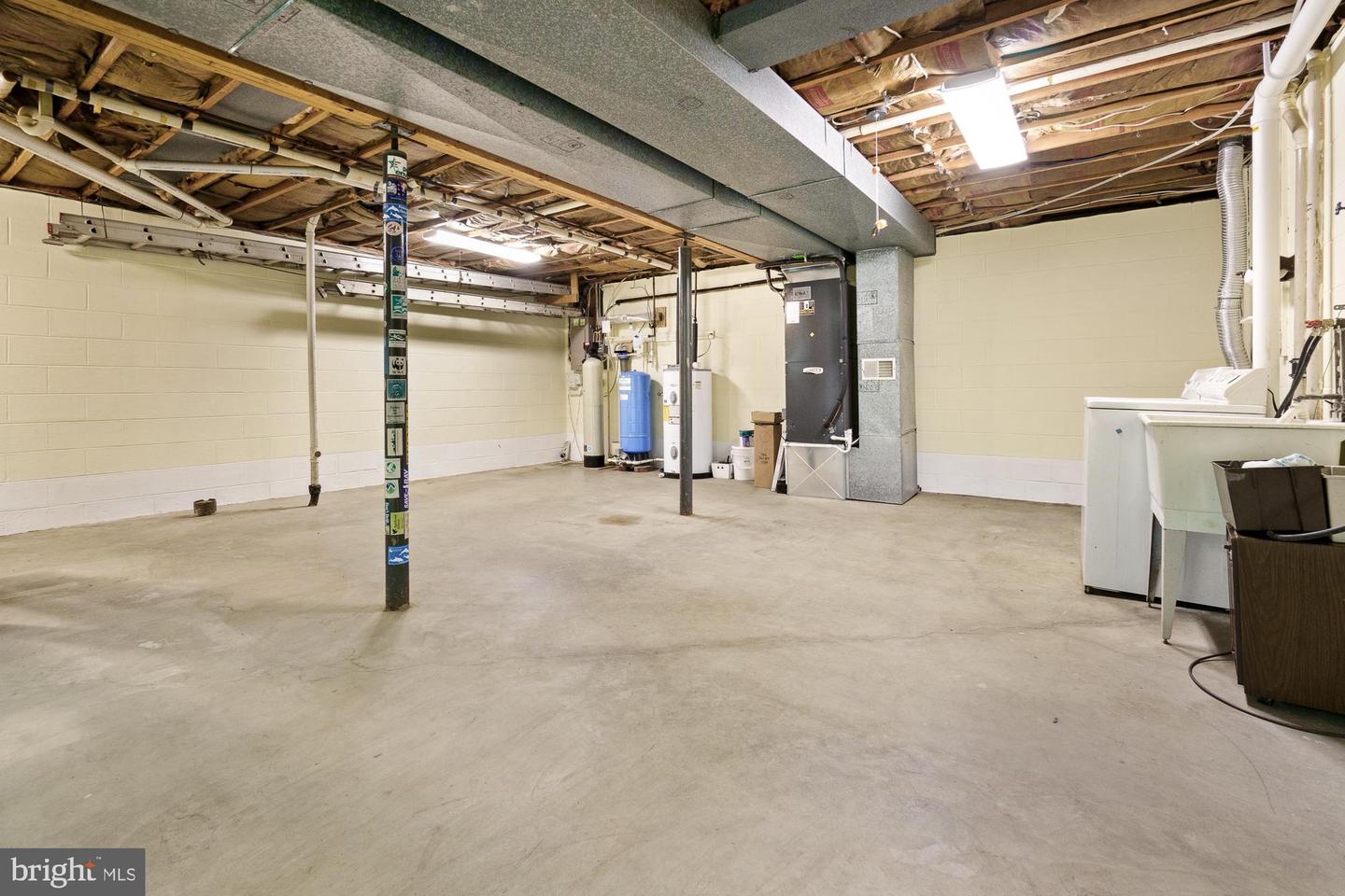 Unfinished basement with exposed joists, mechanical equipment, and laundry appliances along one wall.