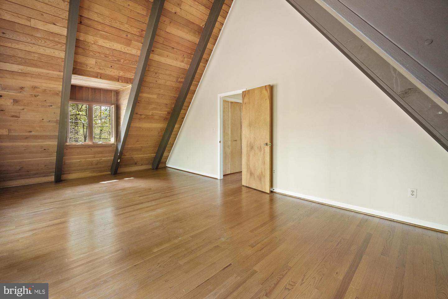 Empty attic room with a vaulted wood ceiling, exposed beams, and hardwood floors.