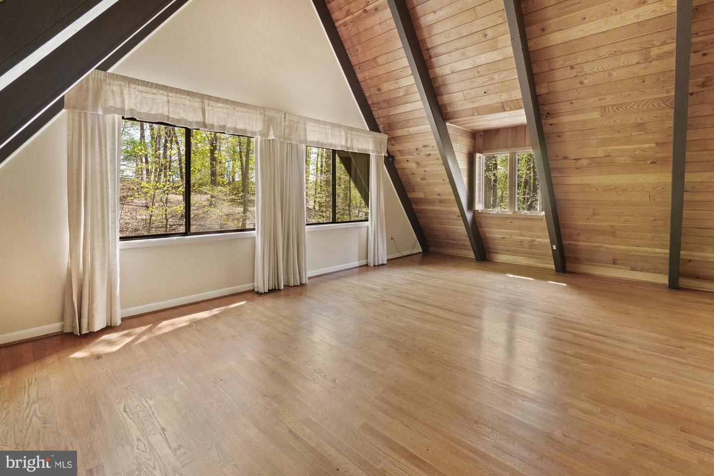 Vacant A-frame room with vaulted wood ceiling, hardwood floors, and large windows overlooking trees.