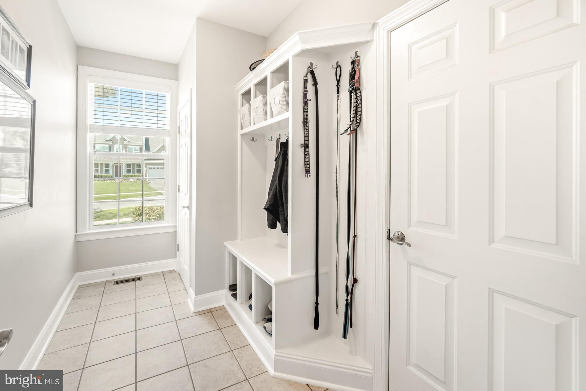 Mudroom with a built-in white bench, cubbies, hanging leashes, and a large window.