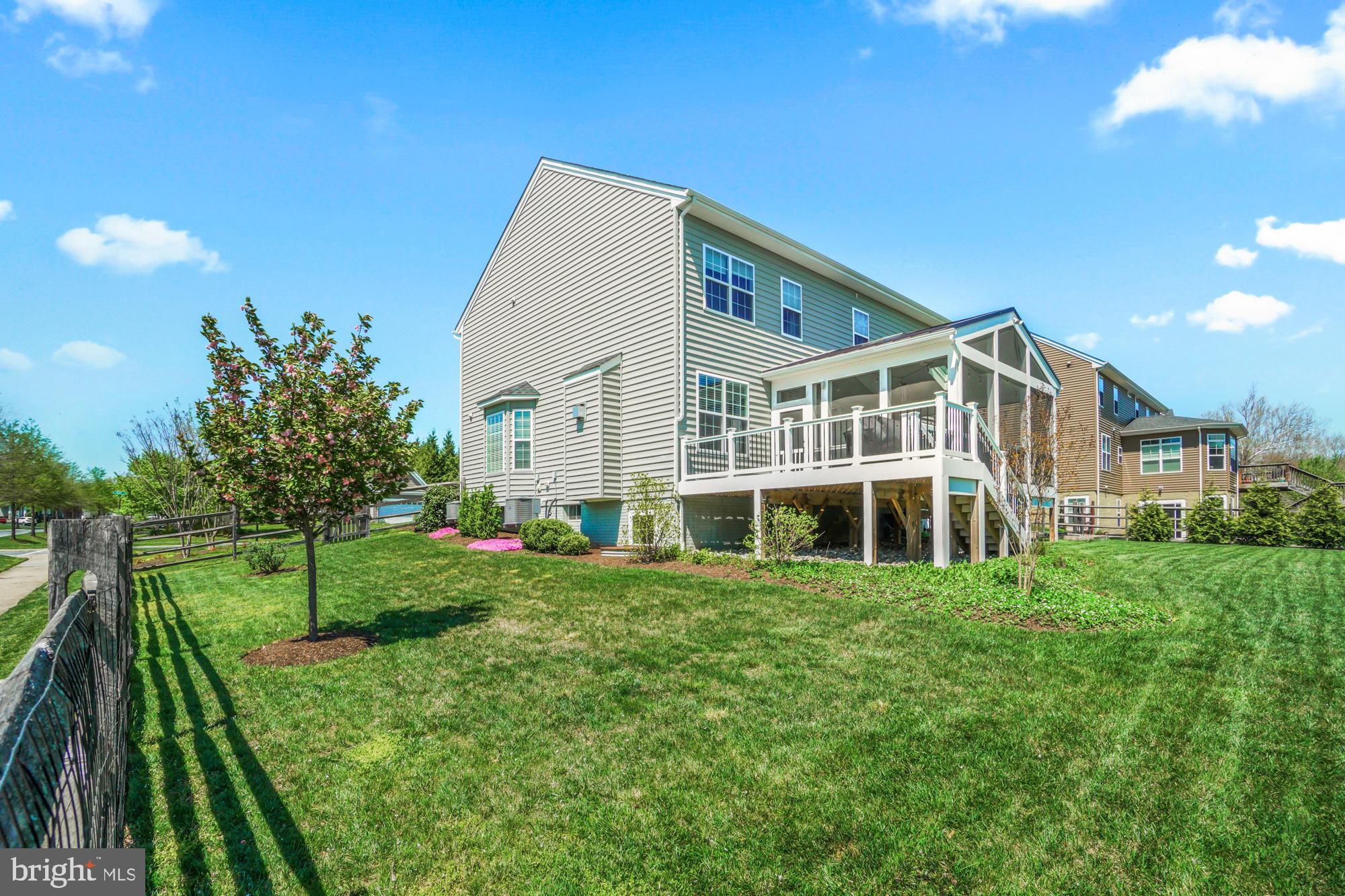 Rear of a two-story home with a raised deck, screened porch, and broad grassy backyard.