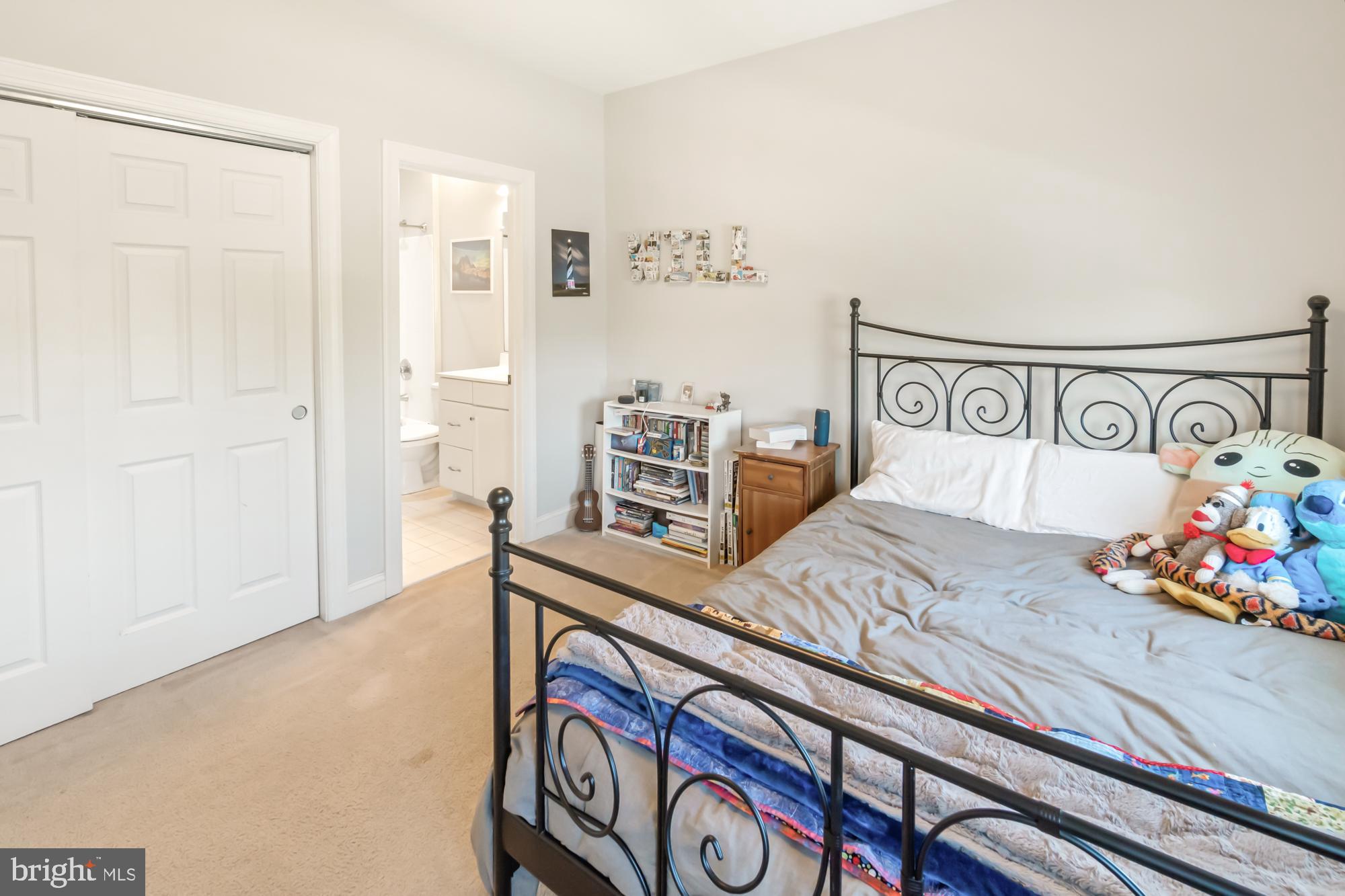 Furnished bedroom with a black metal bed, gray bedding, colorful stuffed toys, and an adjoining bathroom doorway.