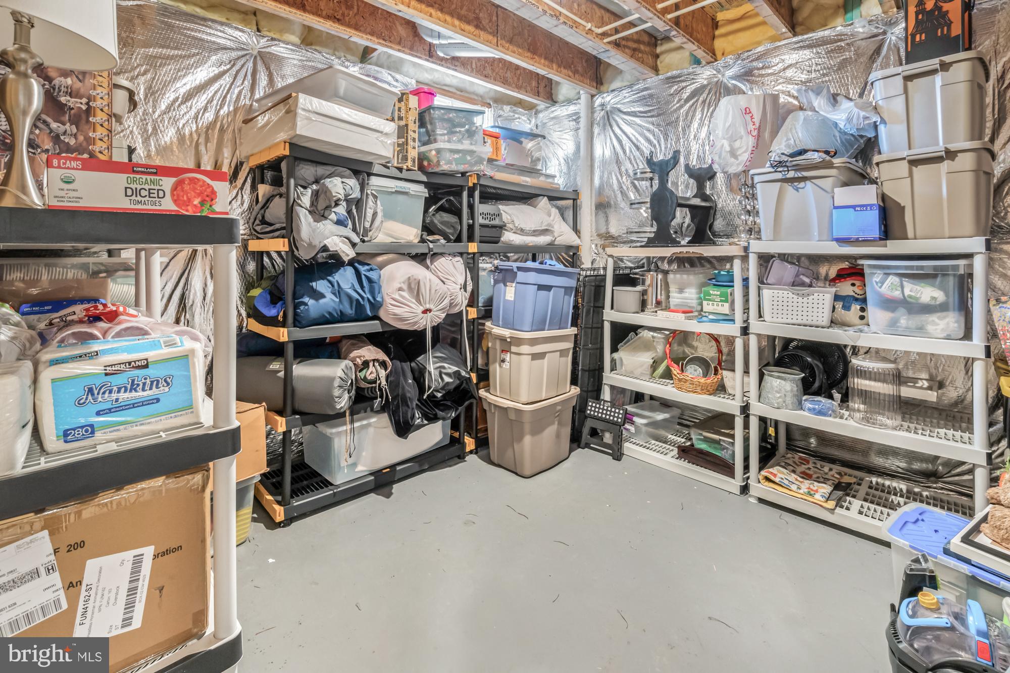 Basement storage area with crowded shelves, stacked bins, and exposed insulated walls and ceiling.
