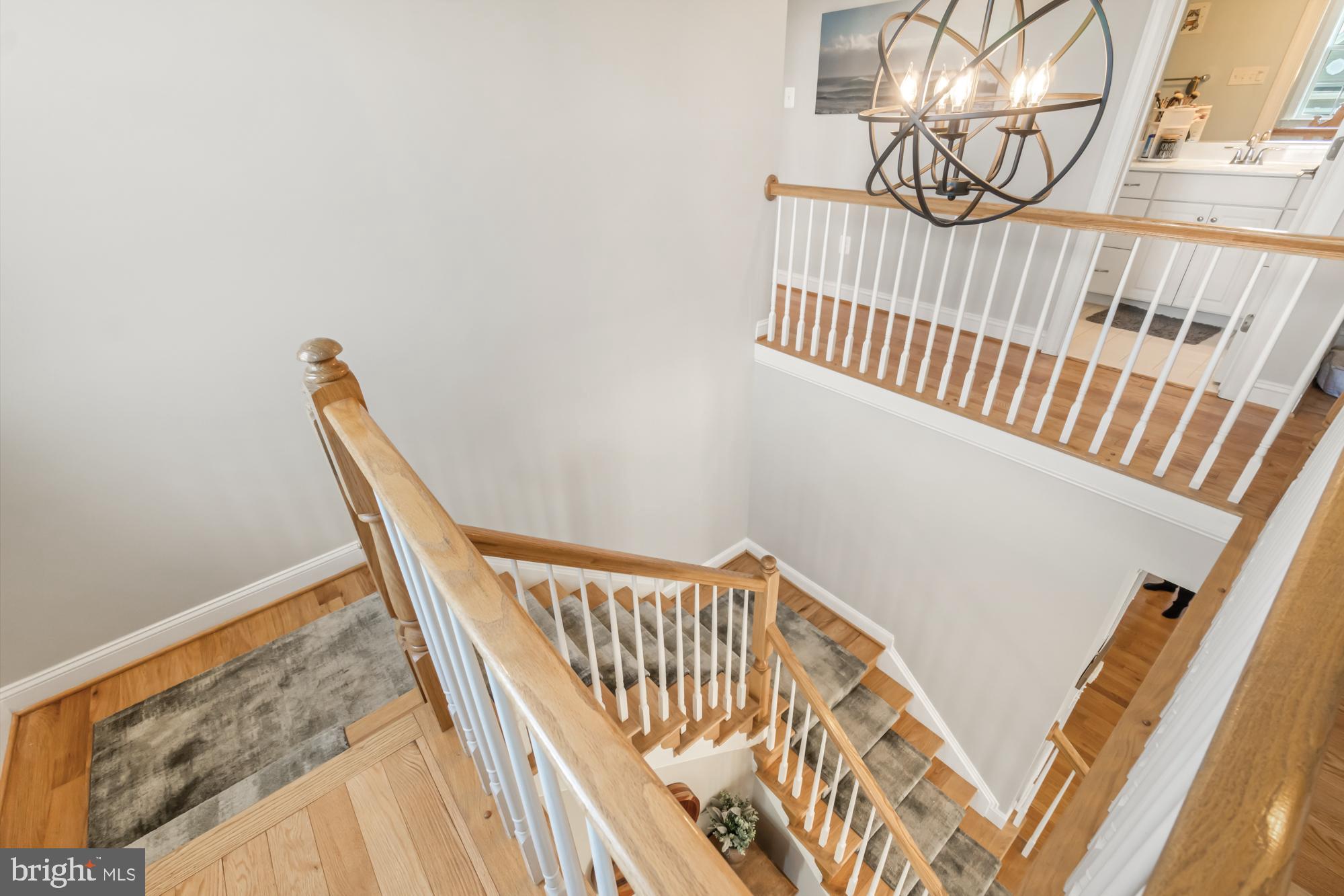 Multi-level staircase with light wood rails, white balusters, gray runners, and a large metal chandelier.