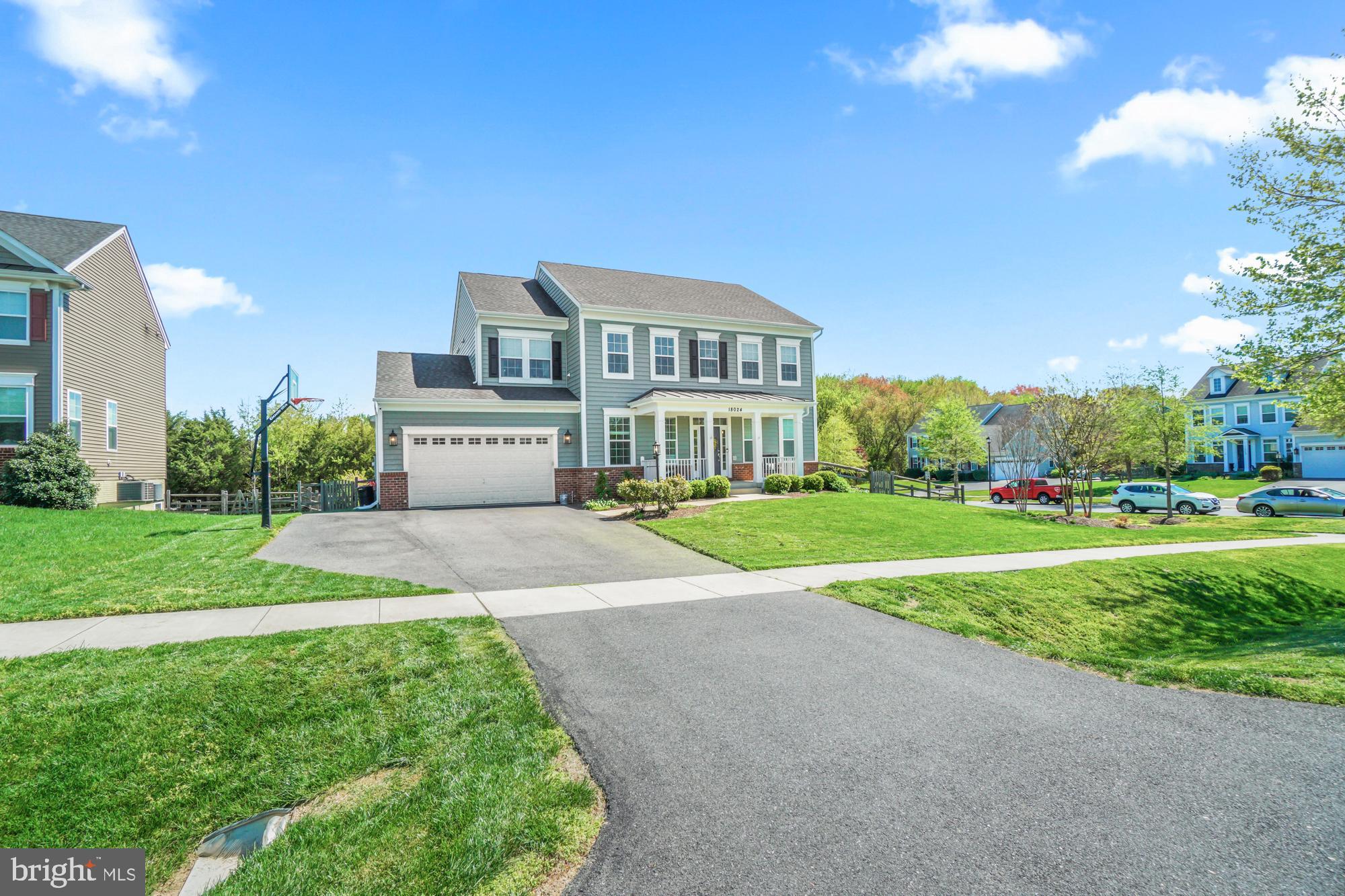 Two-story green house with an attached garage, covered porch, broad driveway, and basketball hoop.