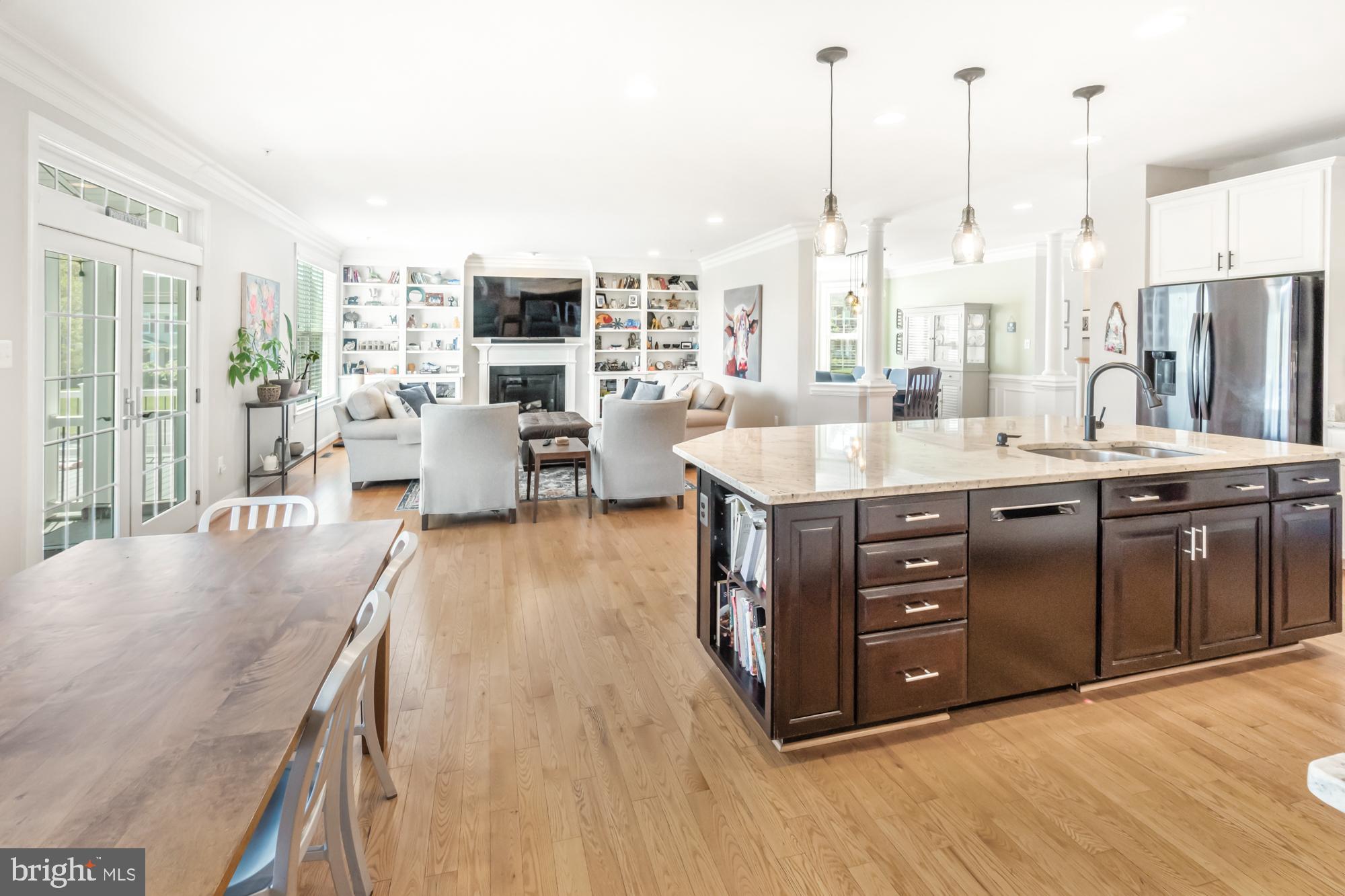 Open-plan kitchen and living area with a large dark island, light wood floors, and built-in shelves around a fireplace.