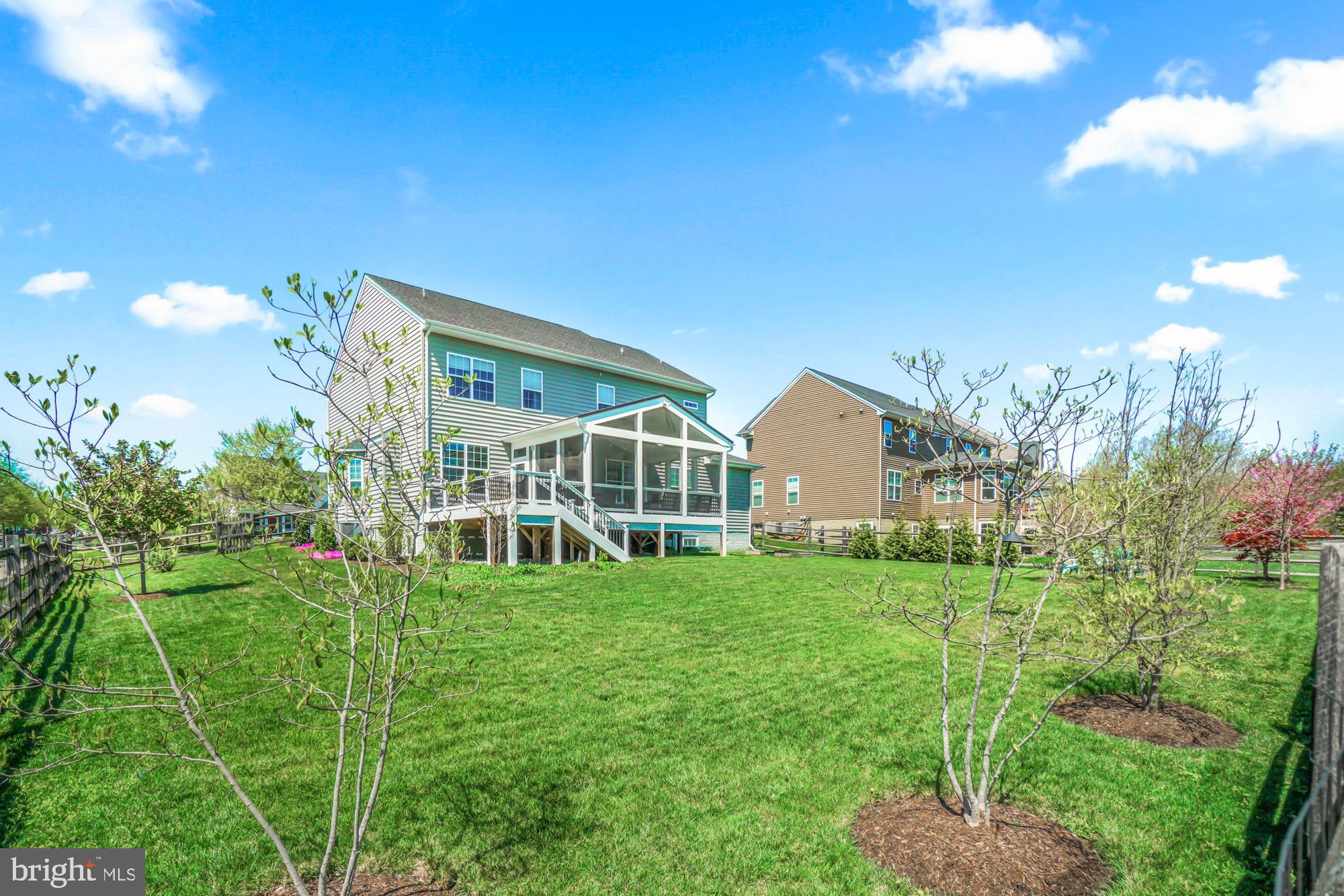 Rear of a two-story house with a raised screened porch overlooking a fenced lawn and young trees.