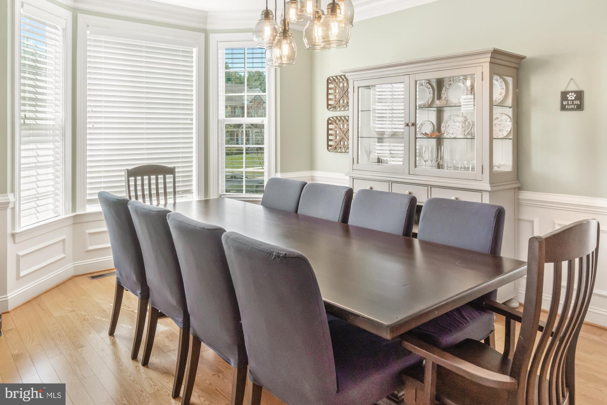 Dining room with a long table, gray upholstered chairs, and a glass-front china cabinet.