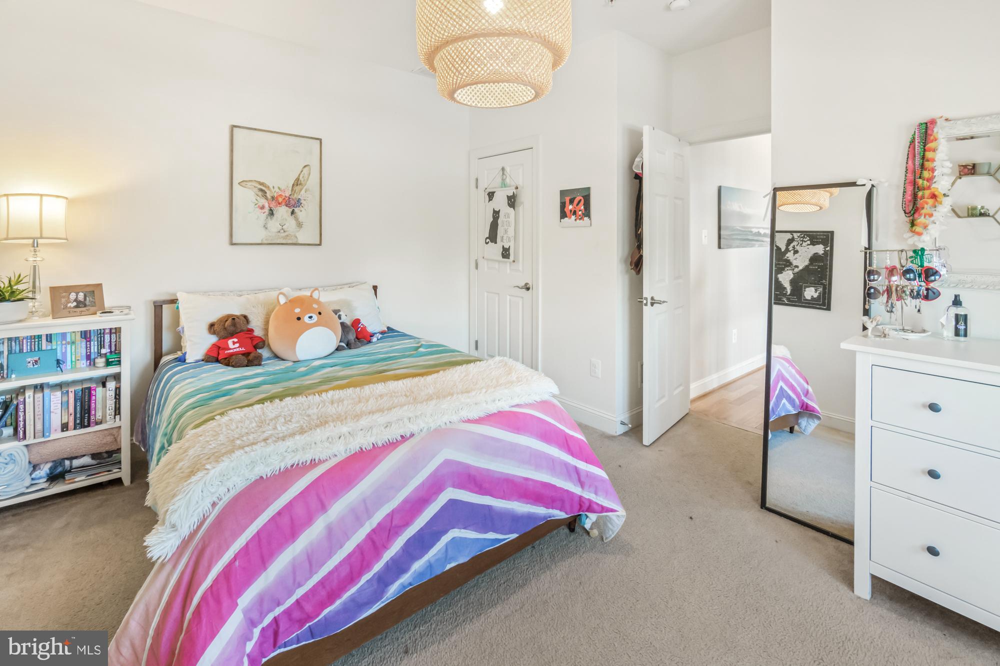 Bedroom with colorful striped bedding, plush toys, and a full-length mirror.