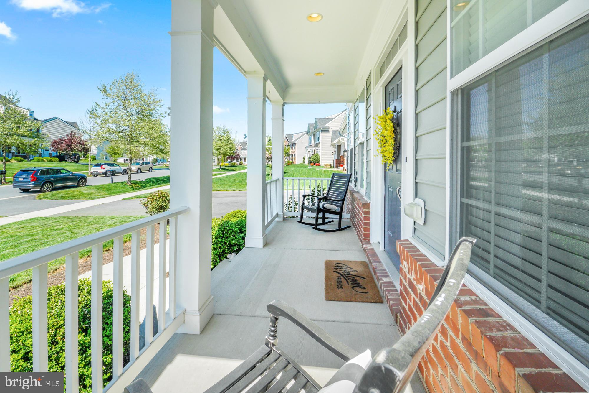 Covered front porch with white columns, brick accents, rocking chairs, and a view of the neighborhood street.