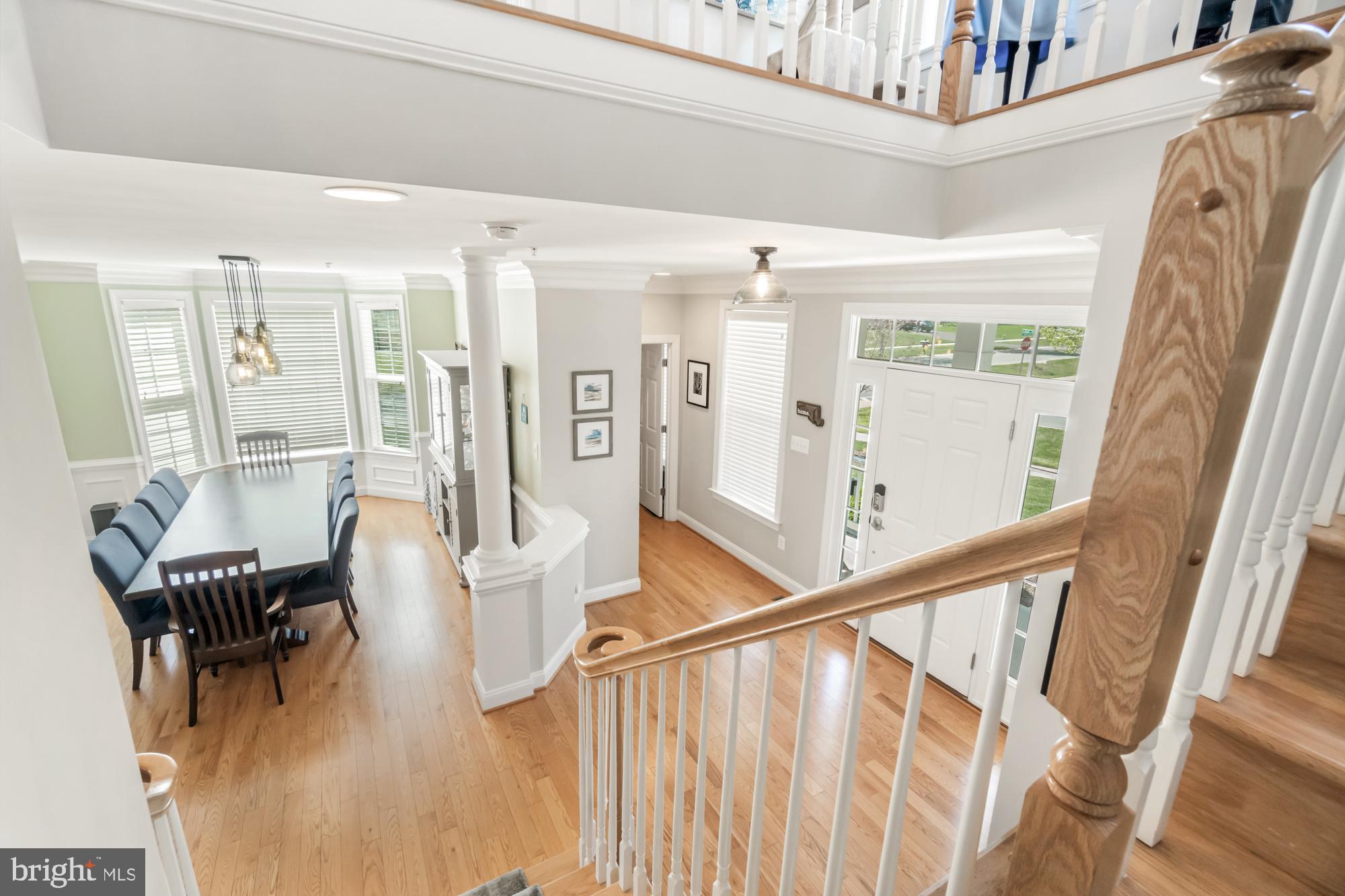 Two-story entry foyer with hardwood floors, white staircase railings, and an adjoining dining area.