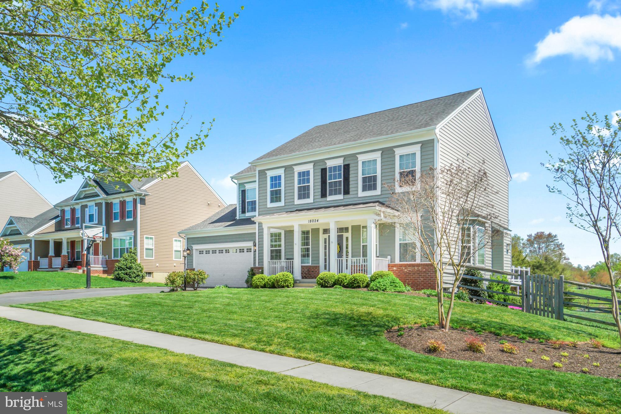 Two-story gray house with a covered porch, attached garage, and landscaped front lawn.