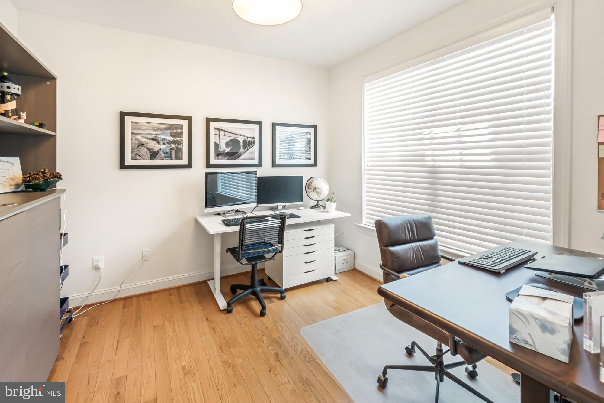 Home office with hardwood floors, computer workstation, and large window with blinds.