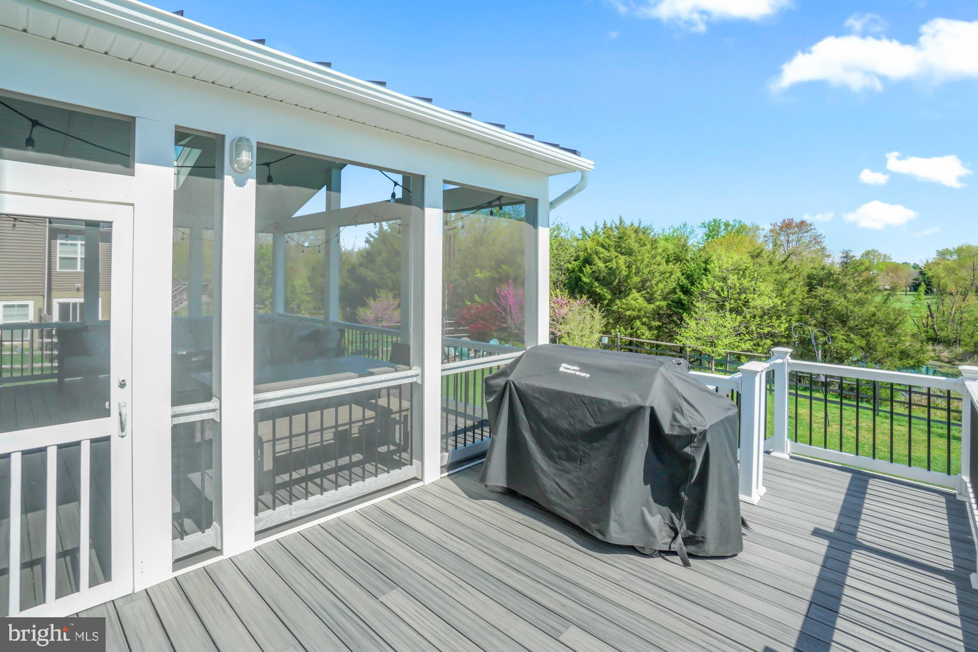 Composite deck beside a screened porch, with a covered grill and leafy backyard beyond the railing.
