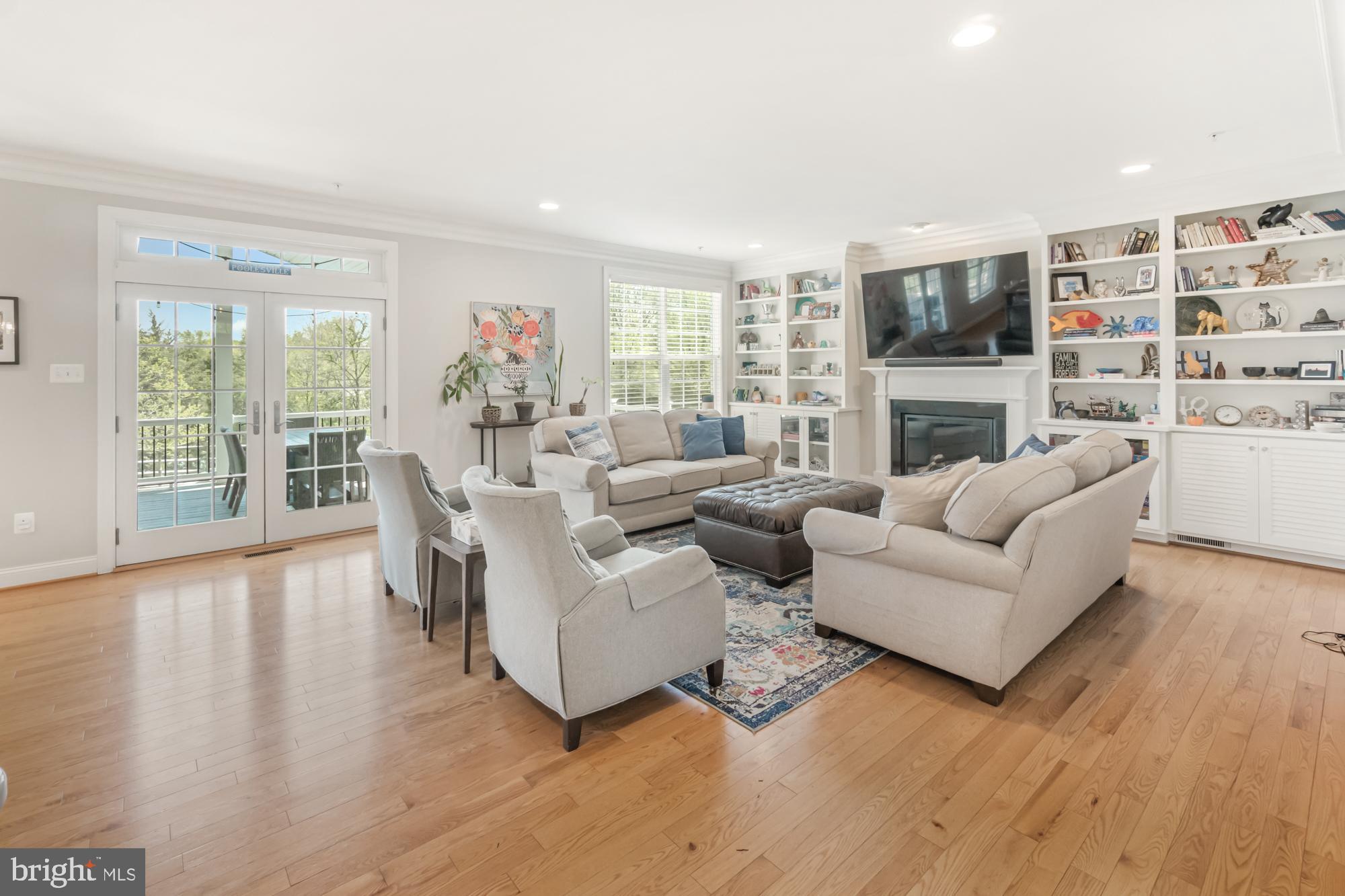 Furnished living room with built-in shelves, fireplace, hardwood floors, and French doors opening to a deck.