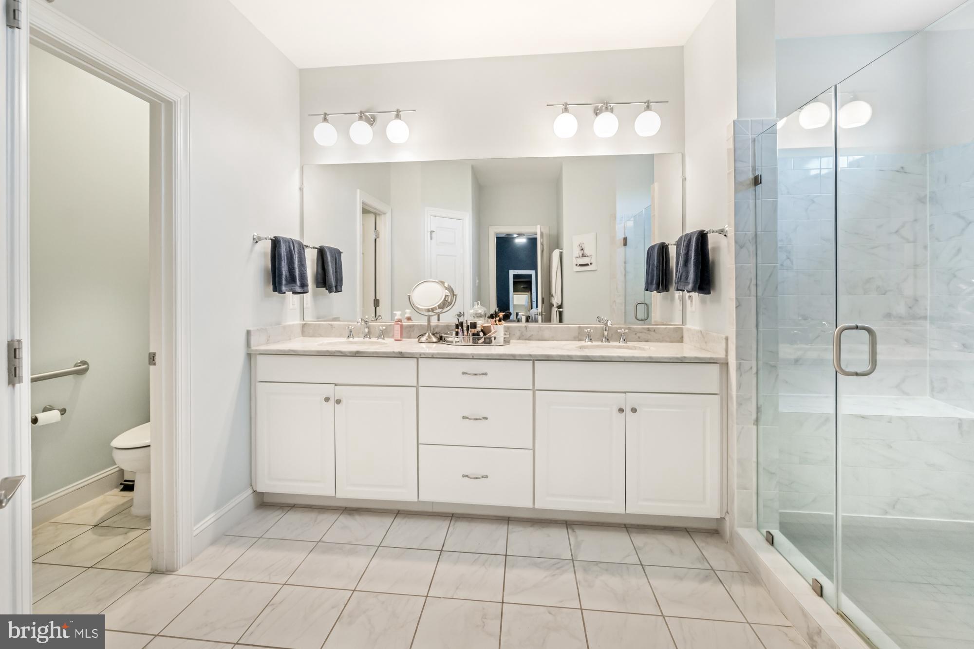Bathroom with a long white vanity, wall-to-wall mirror, and glass-enclosed marble-look shower.