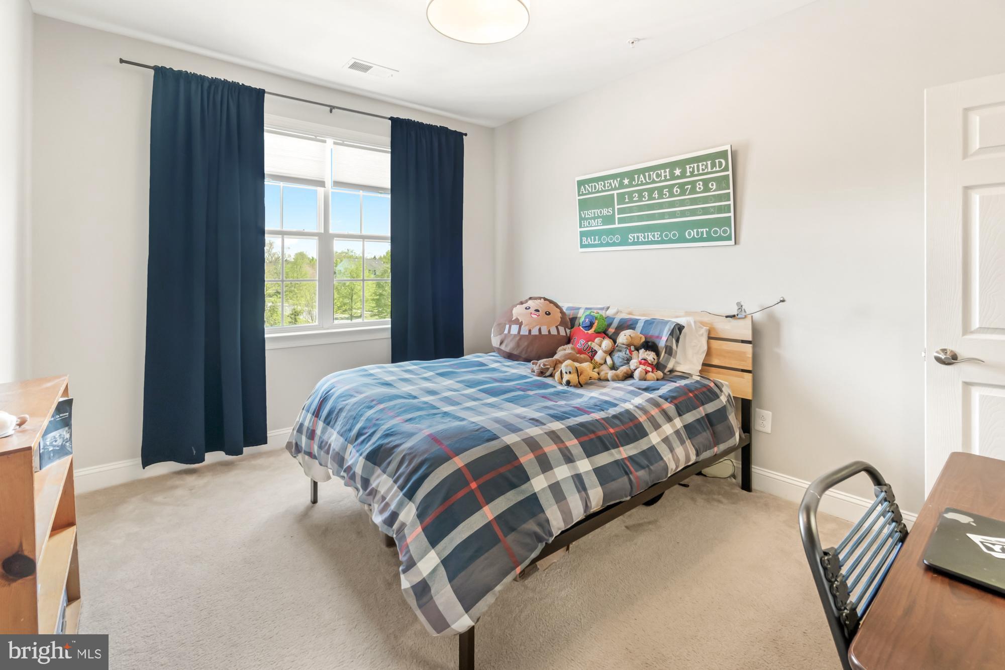 Bedroom with blue plaid bedding, stuffed toys, navy curtains, and a baseball scoreboard.