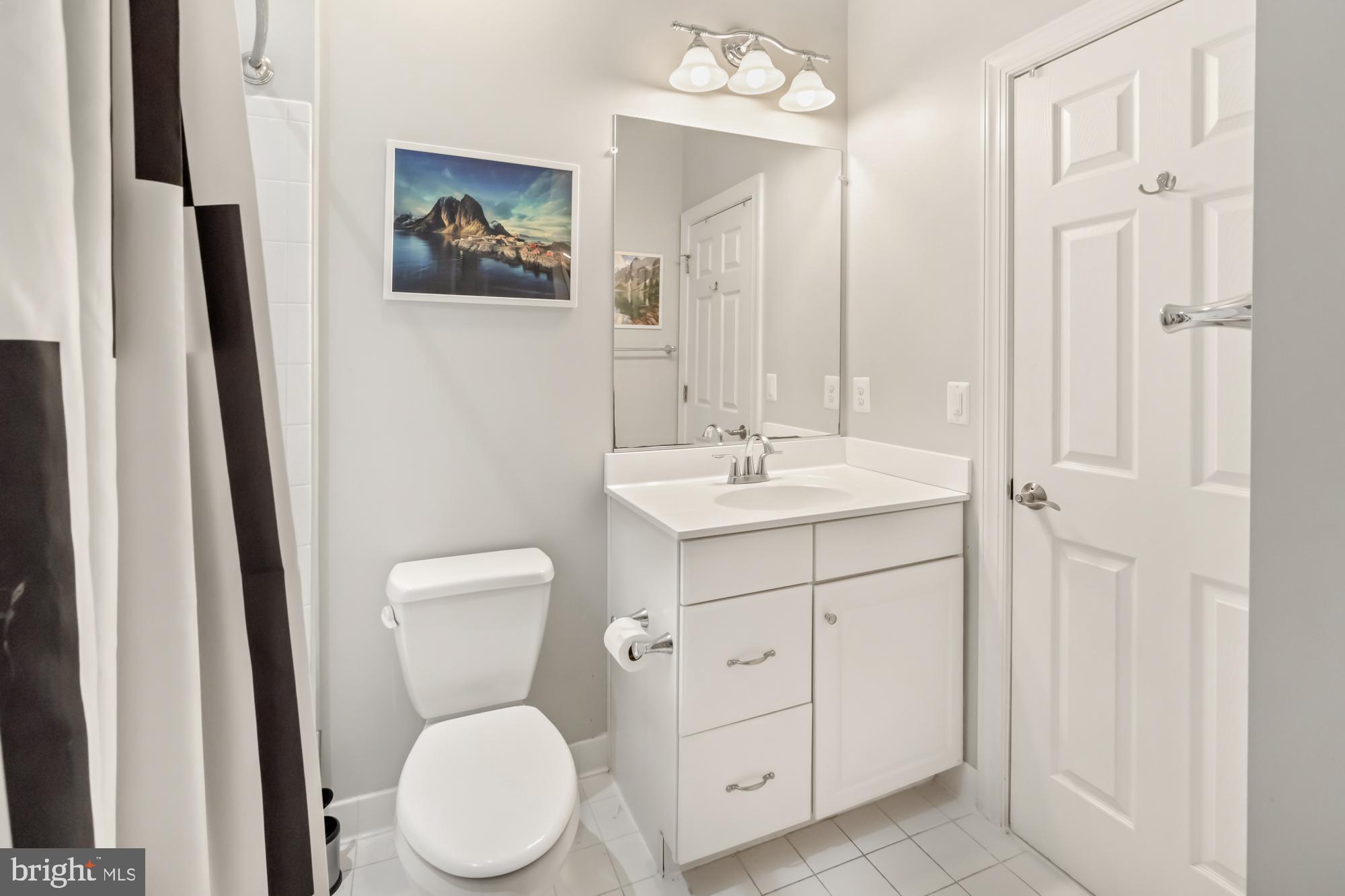 Bathroom with a white vanity, mirrored cabinet, toilet, and black-and-white shower curtain.