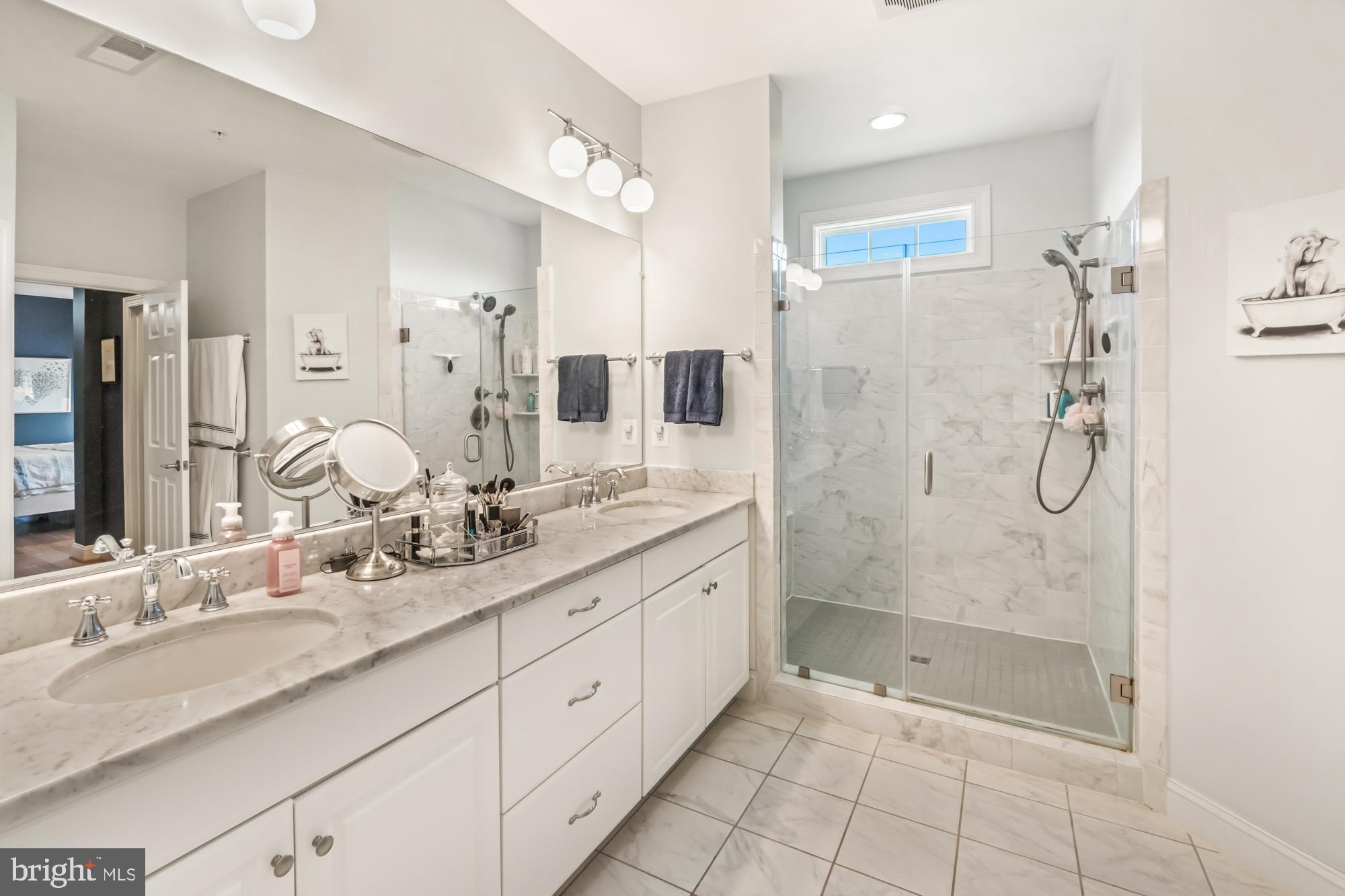 Bathroom with a long marble-look vanity and glass-enclosed walk-in shower.
