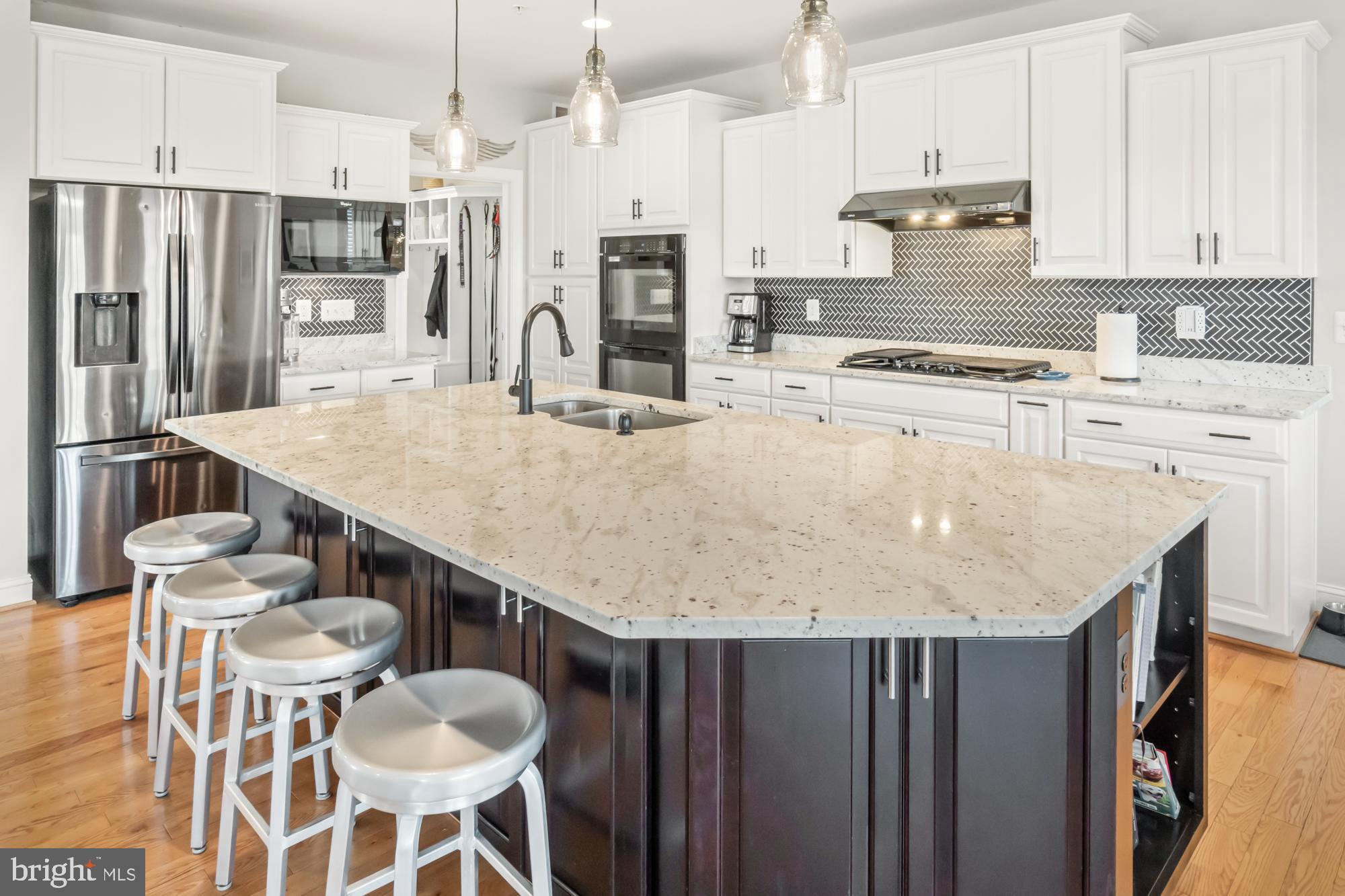 Kitchen with a large stone-topped island, four stools, white cabinets, and stainless steel appliances.