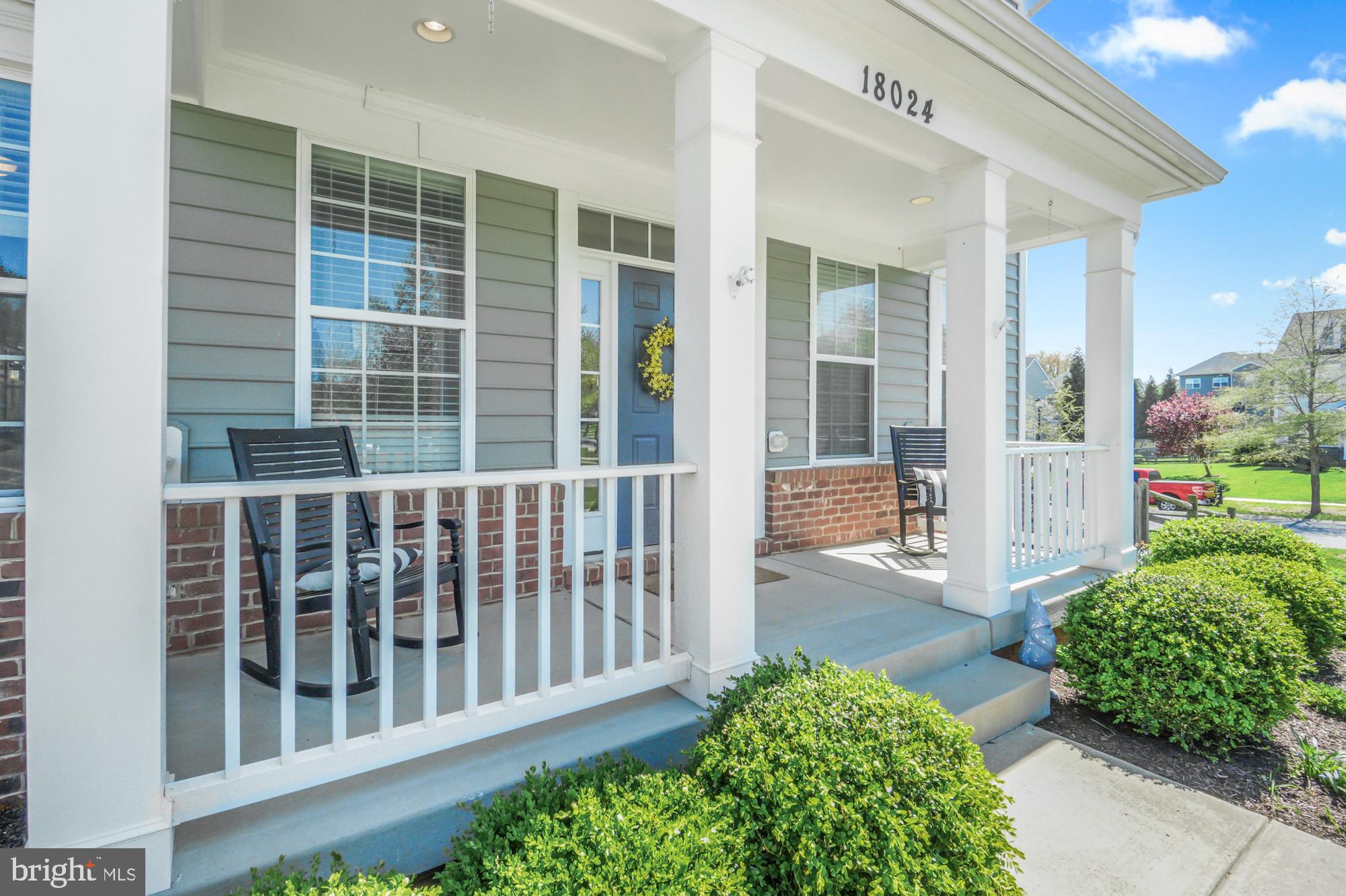 Home front porch with white columns, brick base, blue door, and rocking chairs.