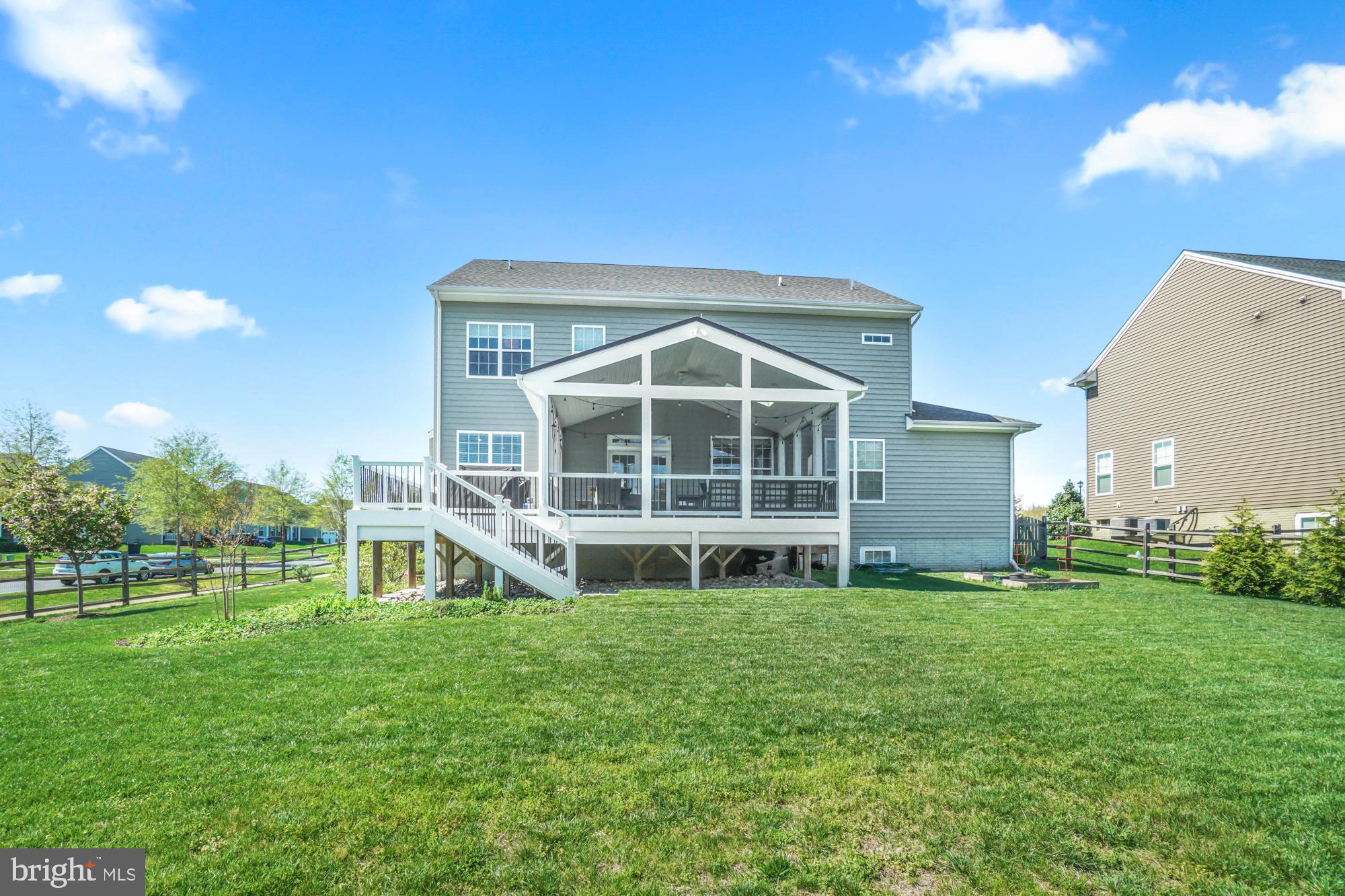 Rear of a gray two-story house with a raised screened porch, deck stairs, and a broad lawn.