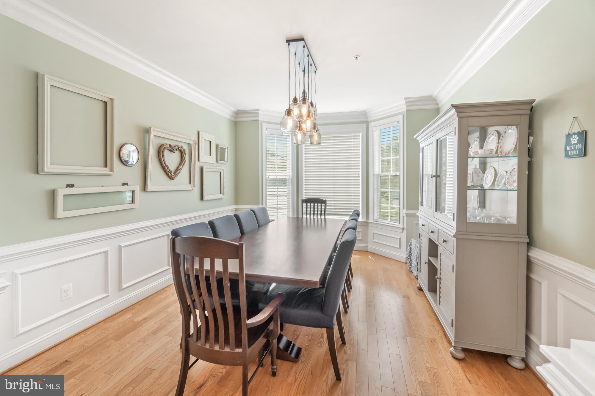 Dining room with a long wood table, shuttered bay windows, and glass-front china cabinet.