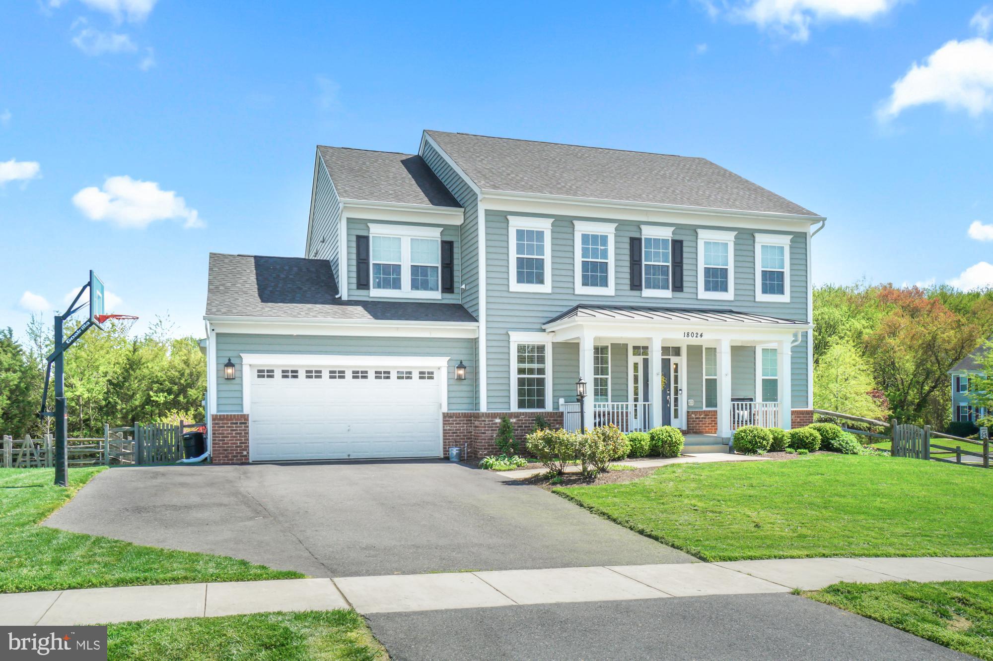 Two-story gray-blue house with a covered porch, attached garage, and basketball hoop by the driveway.