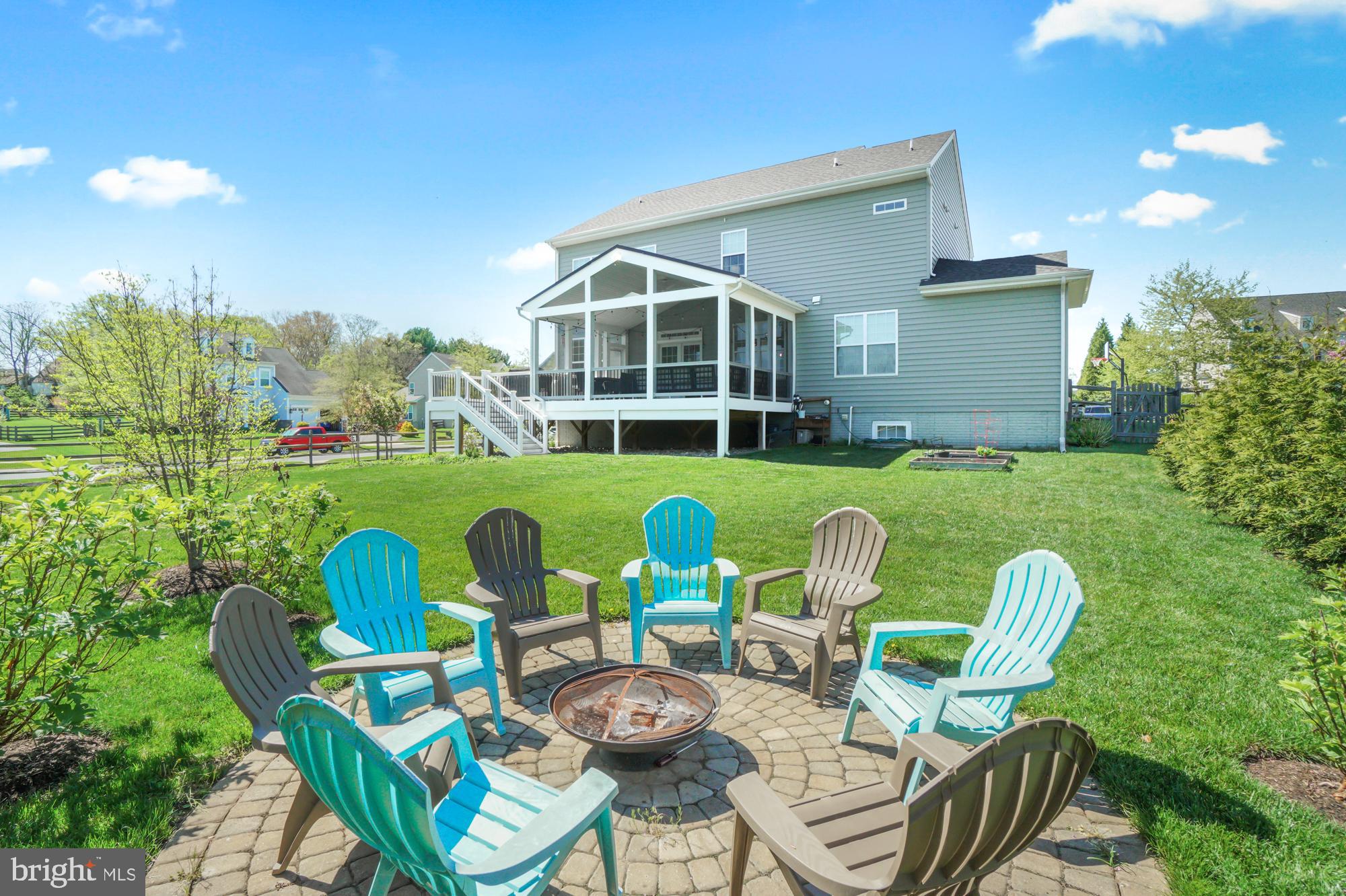 Rear of a gray two-story home with a screened porch and a stone patio with chairs and fire pit.