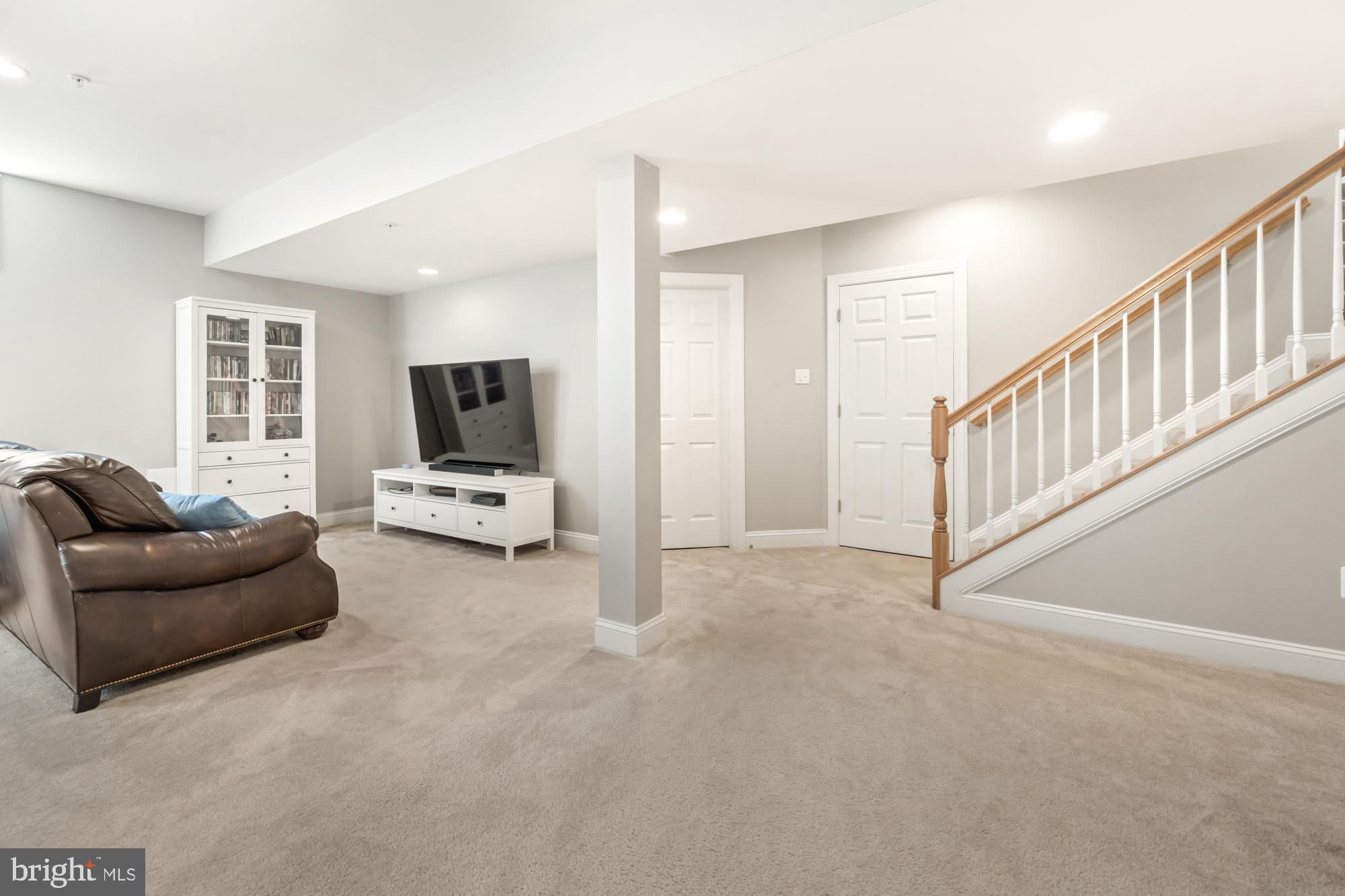 Finished basement family room with carpet, leather sofa, media cabinet, and staircase.