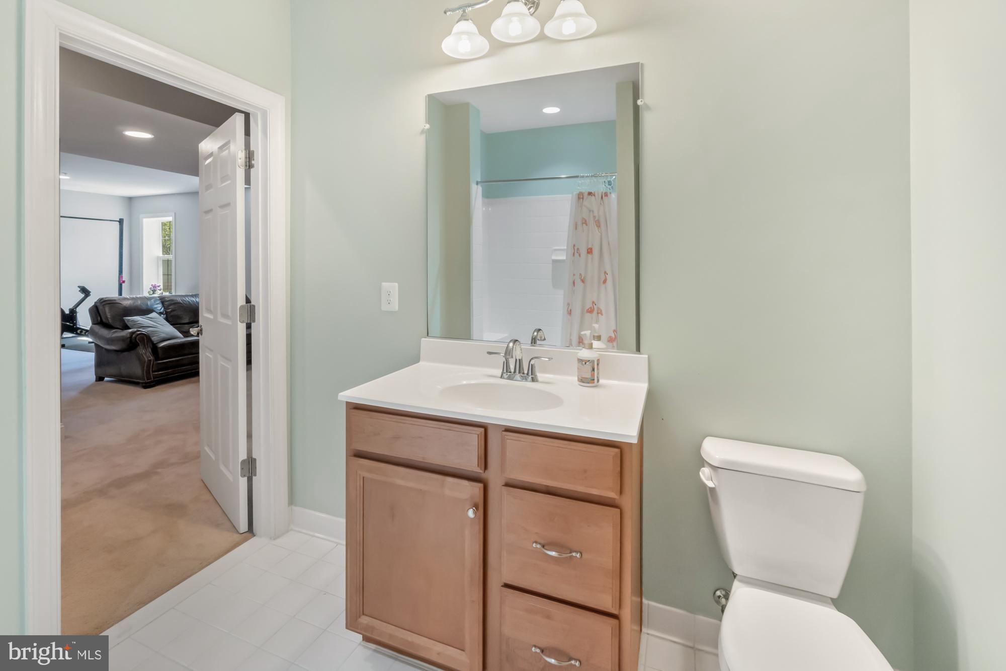 Bathroom with a wooden vanity, large mirror, and doorway to a furnished room.