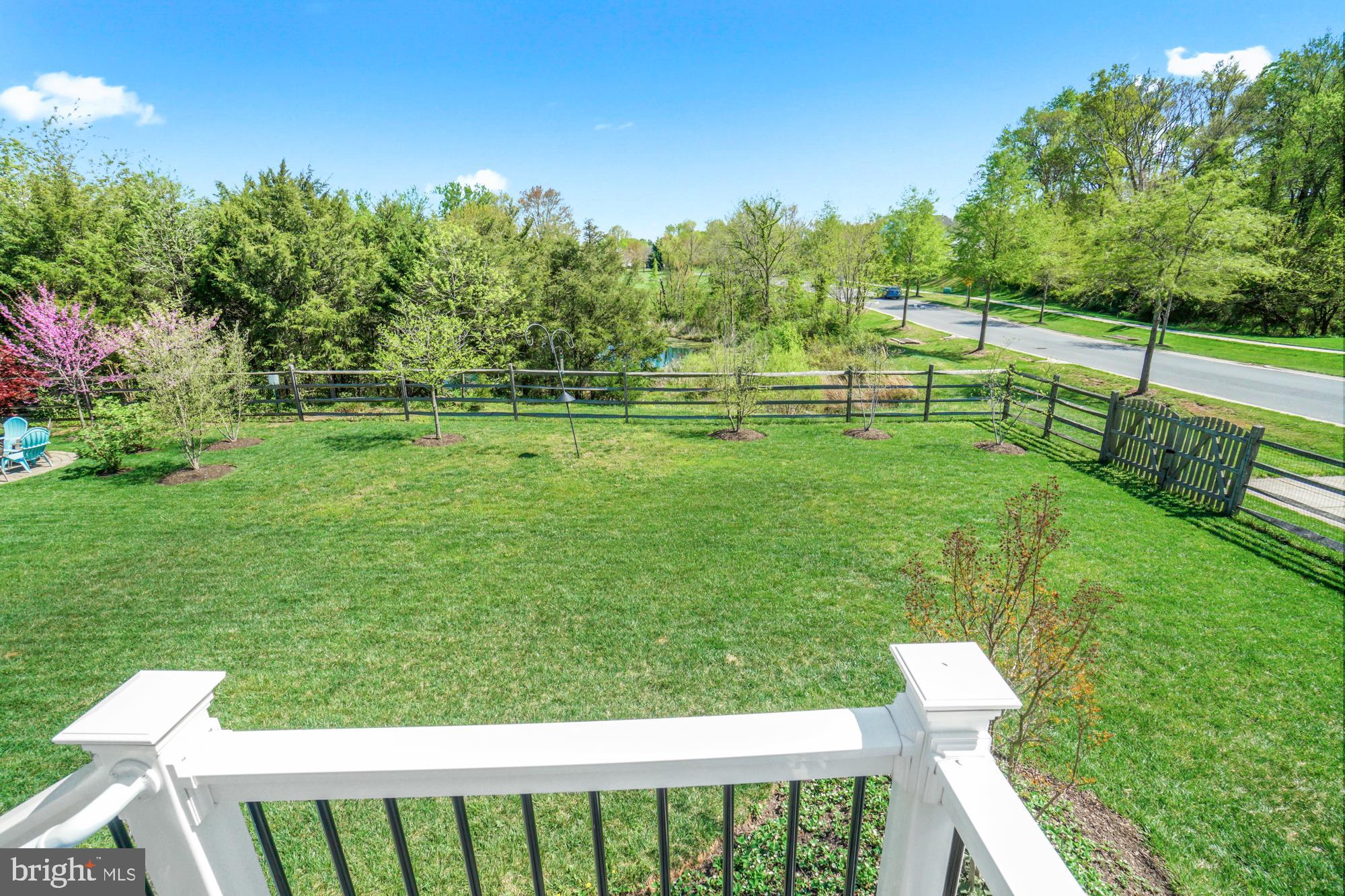 Fenced backyard with a broad lawn, young trees, and a wooded area beyond.