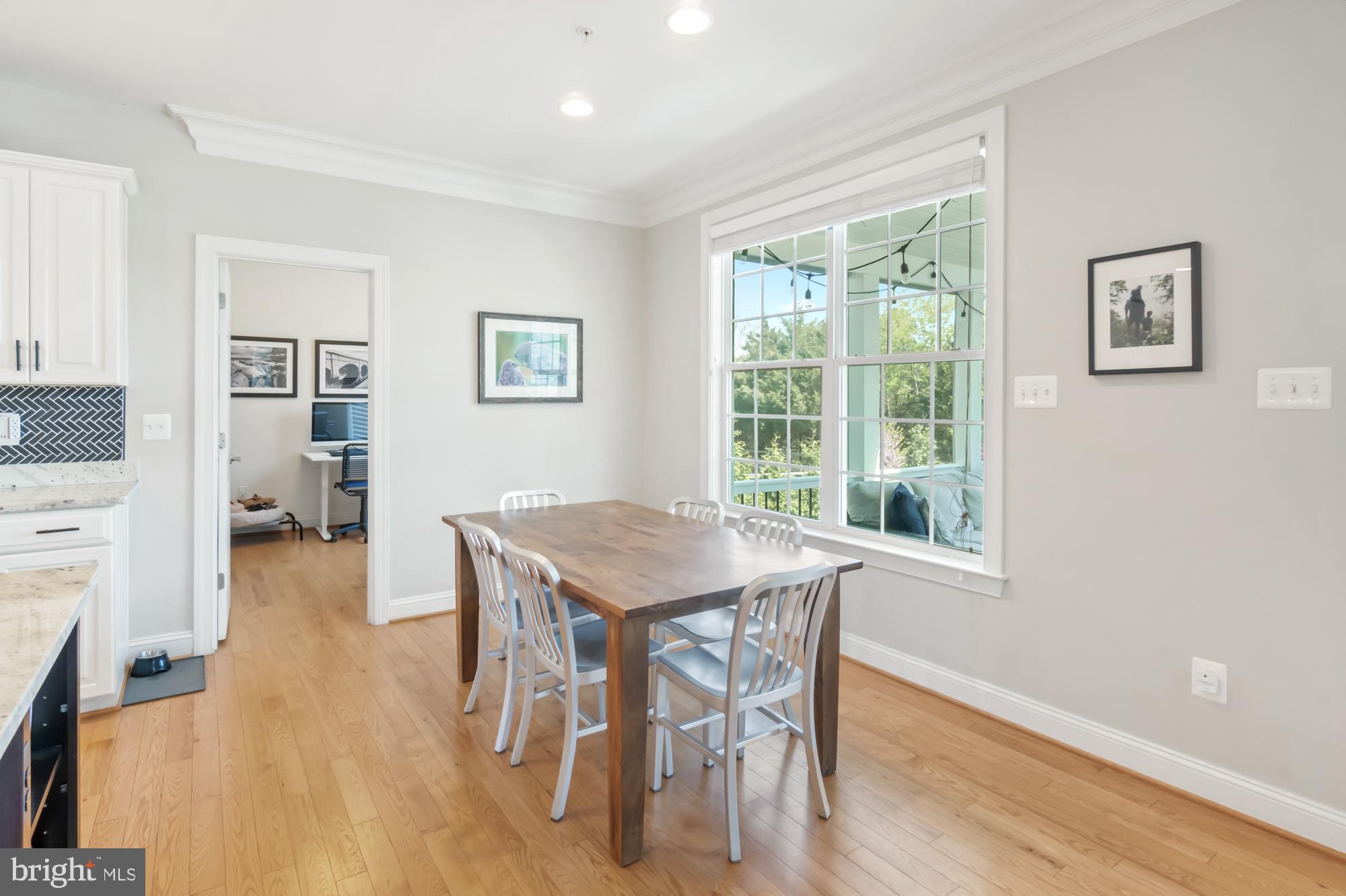 Dining area with a wooden table and white chairs beside a large window overlooking trees.