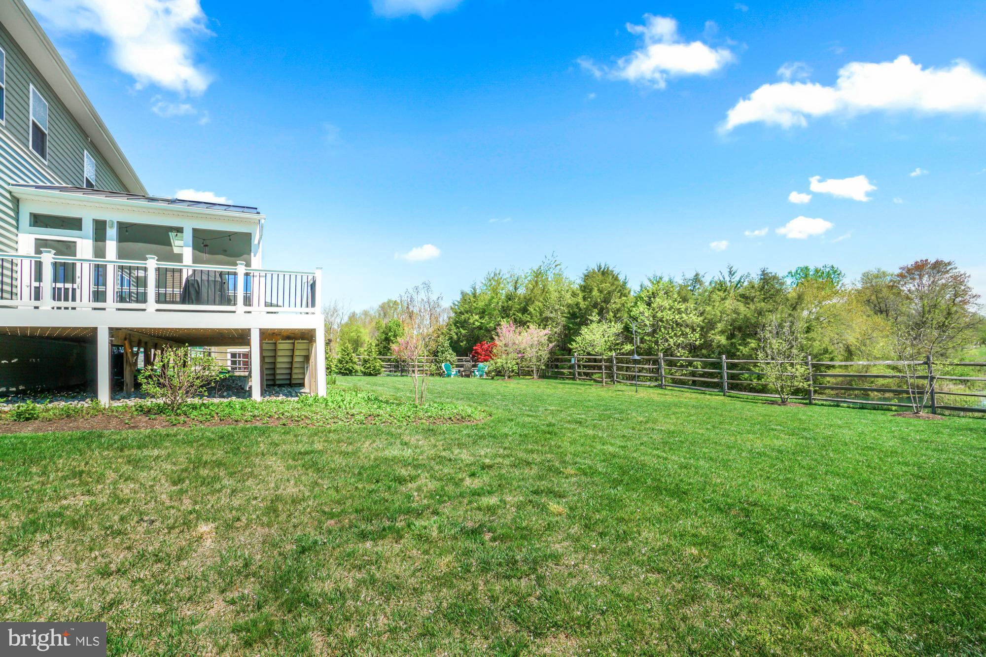 Home’s rear deck and covered patio beside a broad fenced lawn and spring trees.