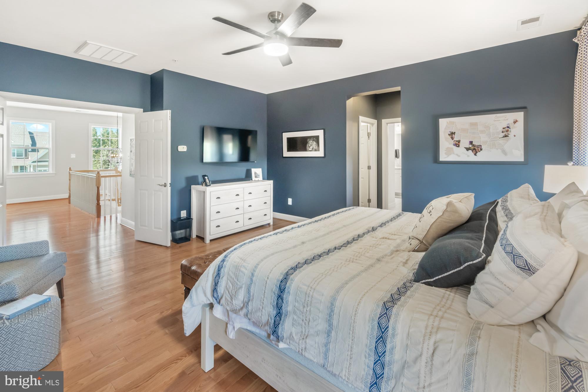 Furnished bedroom with blue walls, patterned bedding, hardwood floors, and an open doorway to the landing.