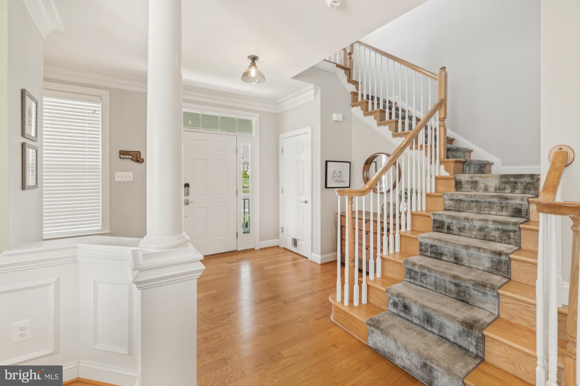 Entry foyer with hardwood floors, a white column, and a wood staircase with a gray carpet runner.