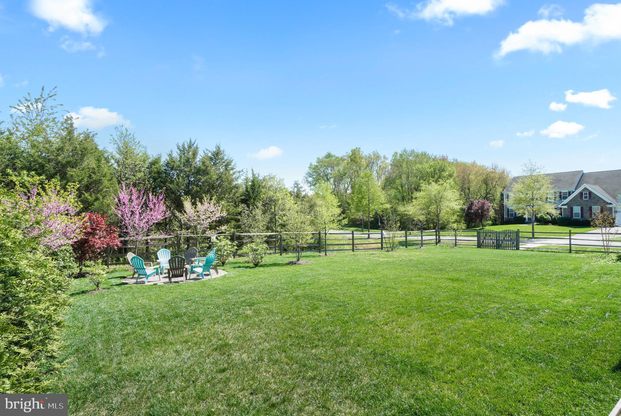 Fenced backyard with a broad lawn, patio chairs, and flowering trees.