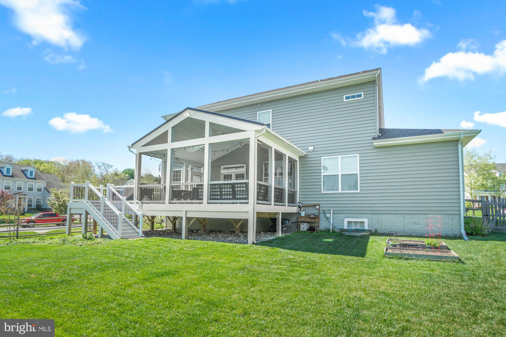 Rear of a two-story gray home with an elevated covered porch and stairs overlooking a broad lawn.