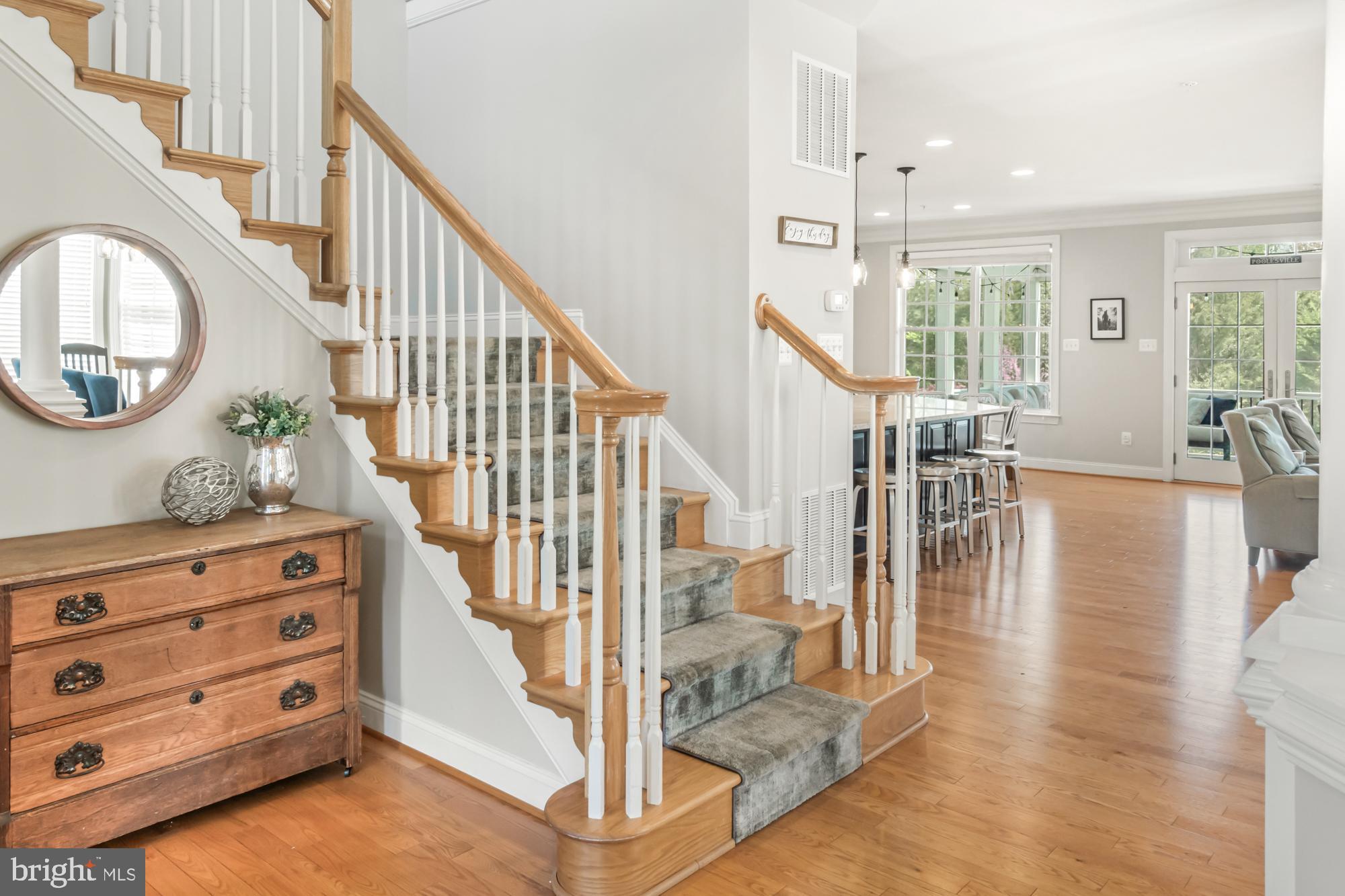 Foyer with carpeted staircase, wood handrails, hardwood floors, and a chest beneath a round mirror.