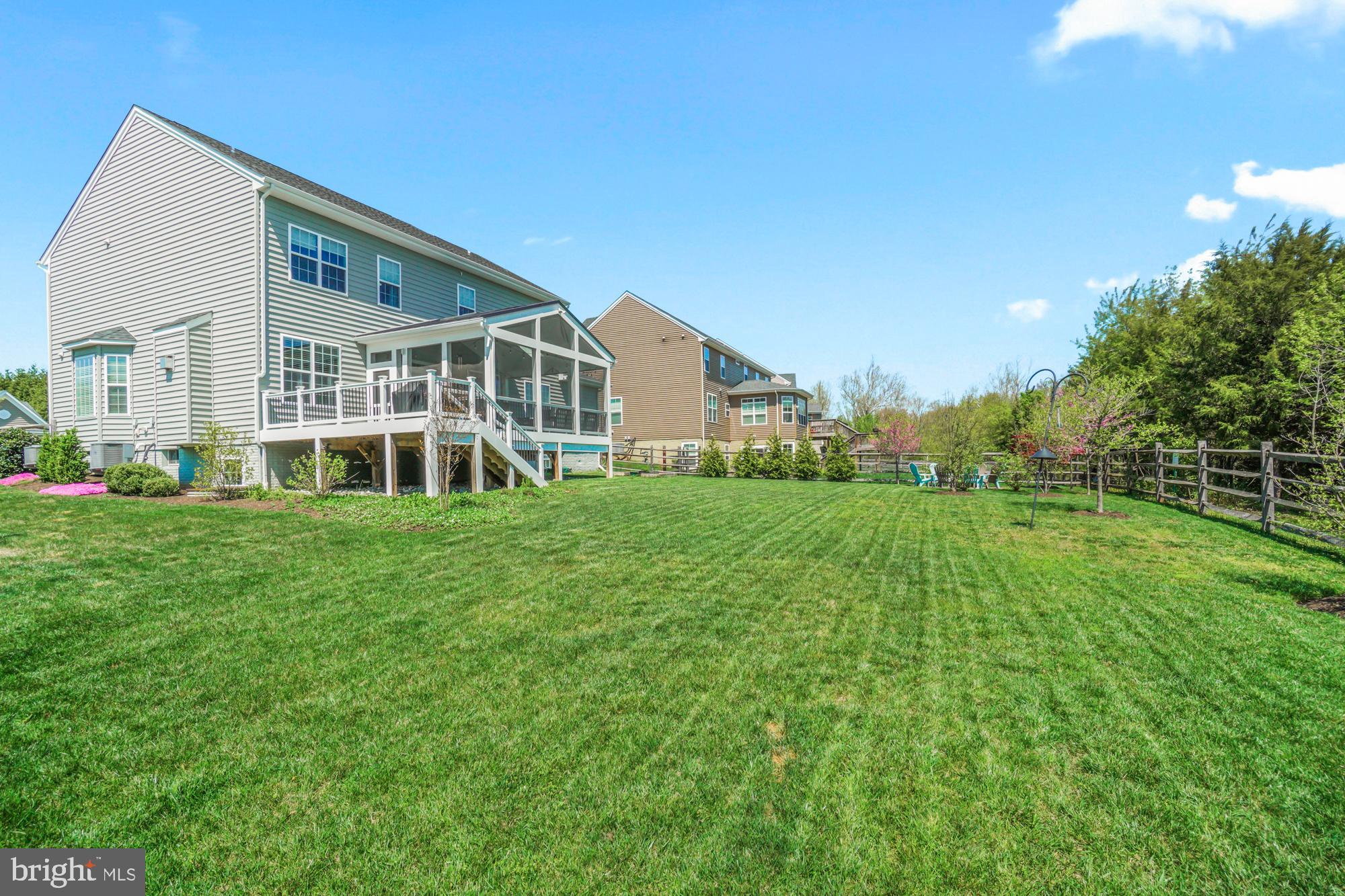 Rear of a gray two-story house with a raised deck and screened porch overlooking a broad fenced lawn.