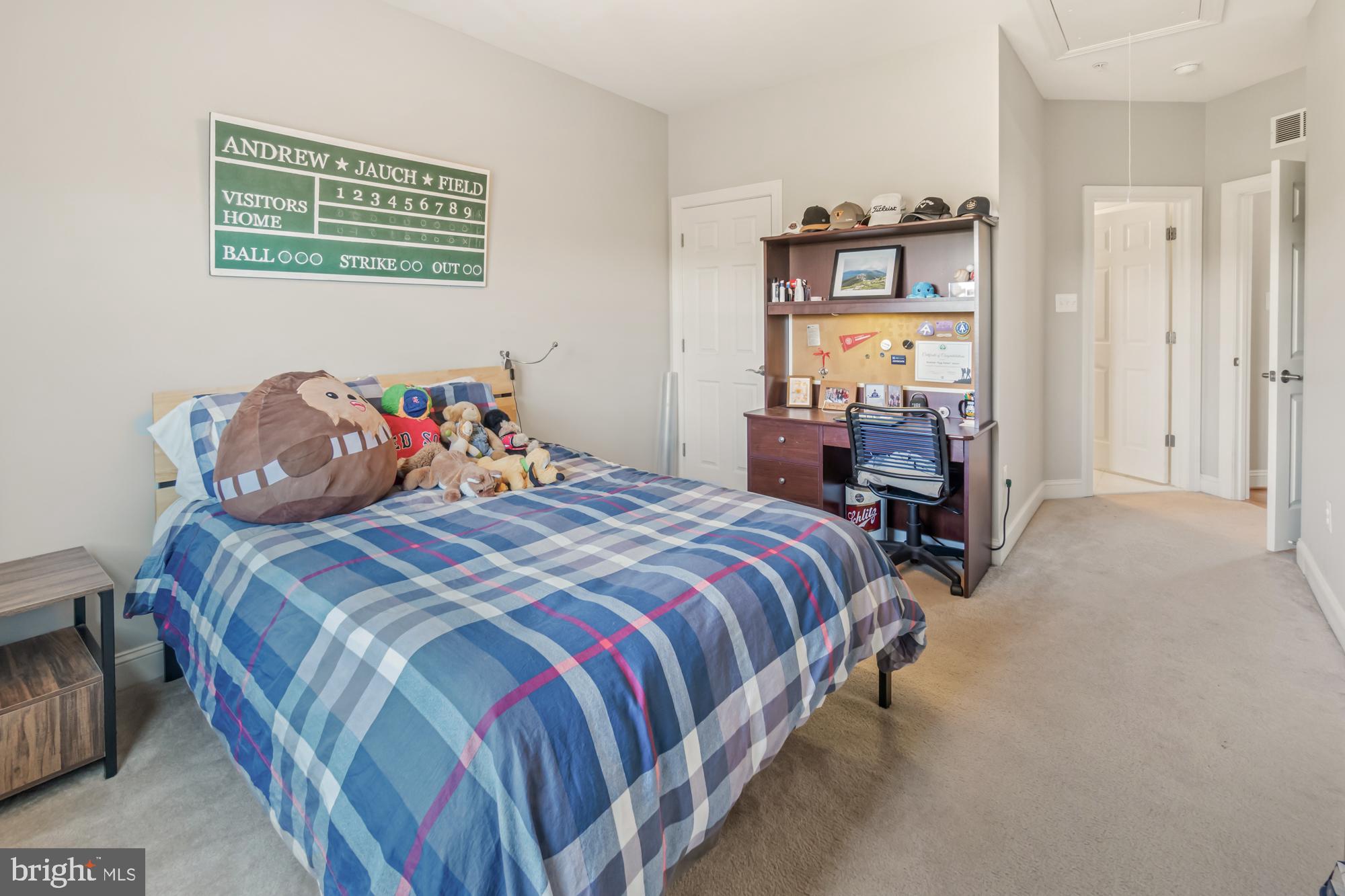 Furnished bedroom with blue plaid bedding, stuffed toys, and a baseball scoreboard above the bed.